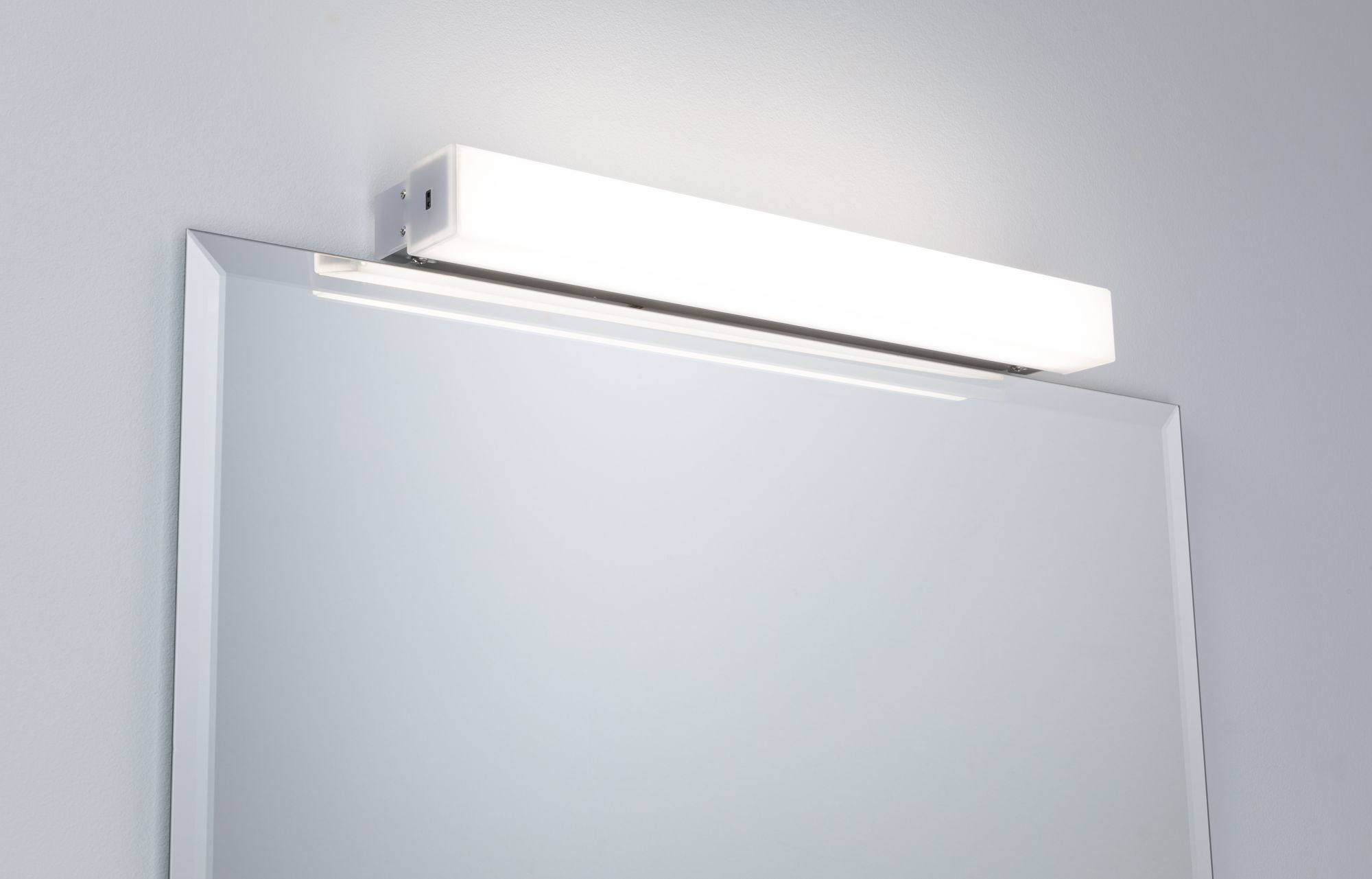 Ein Spiegel mit einer horizontalen LED-Leuchte darüber an einer grauen Wand.