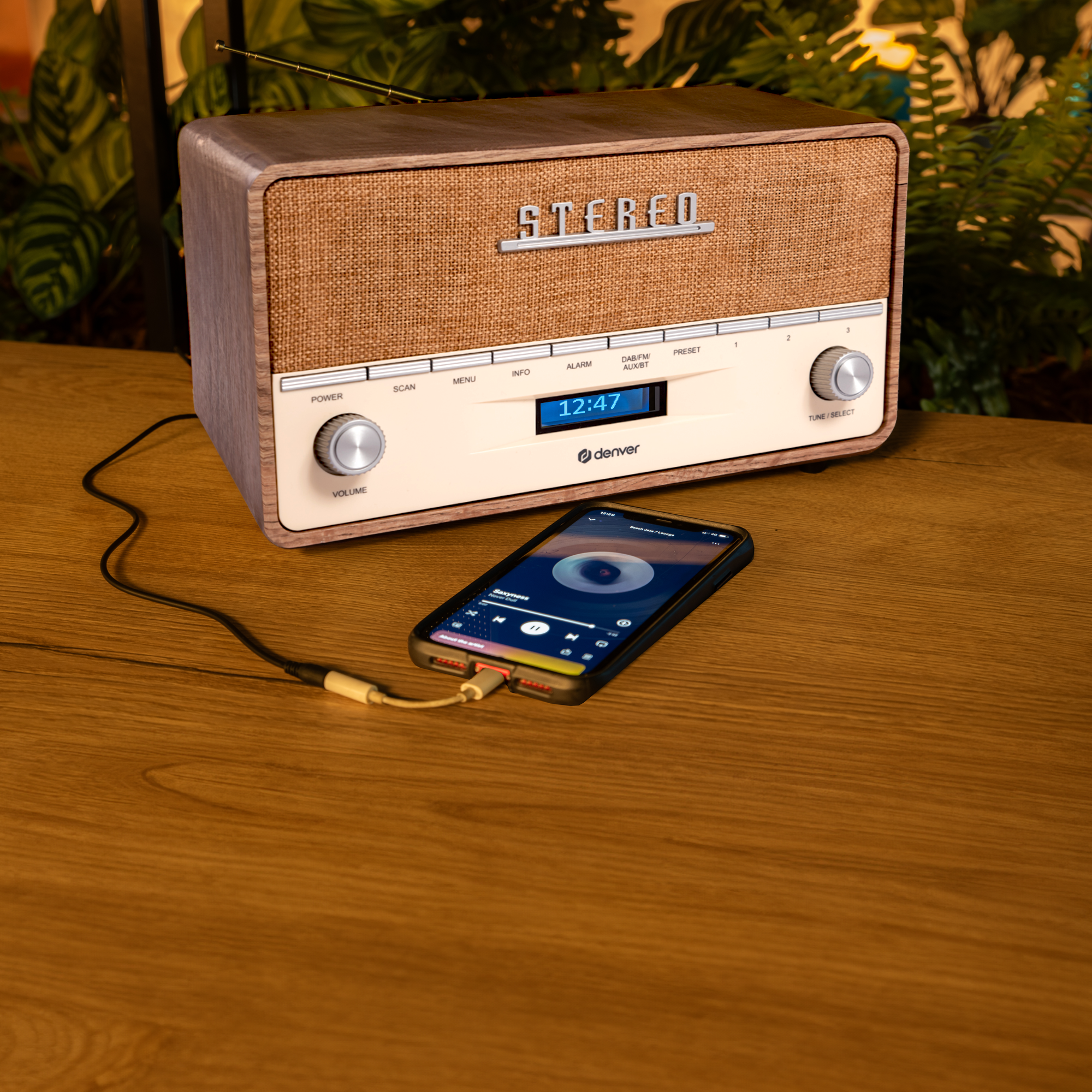 Radio w stylu vintage stoi na drewnianym stole. Telefon jest z nim połączony kablem.