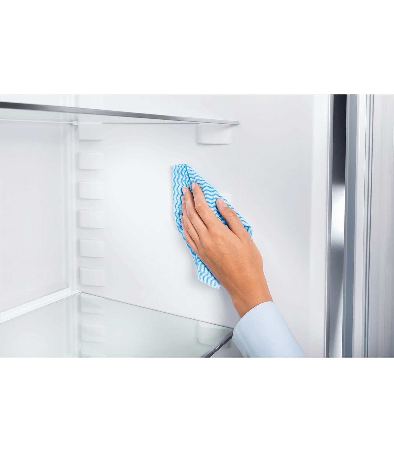 Una mano con un panno blu e bianco che pulisce l'interno bianco di un frigorifero.