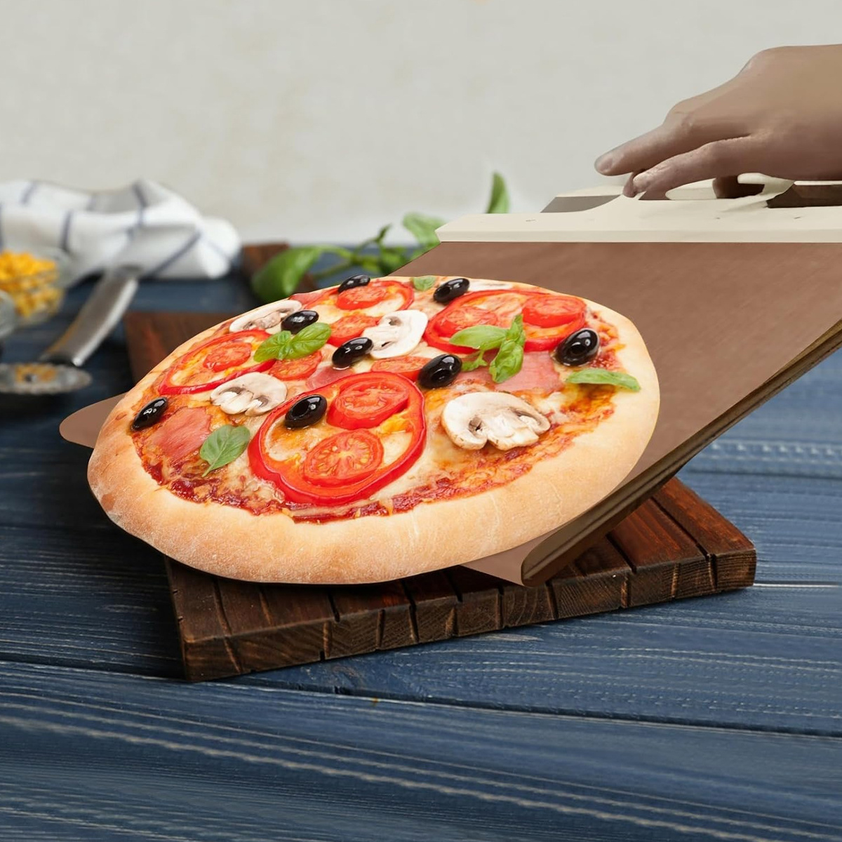 Eine Pizza auf einem Holzbrett mit Gemüse, jemand legt einen hölzernen Pizzaschneider.