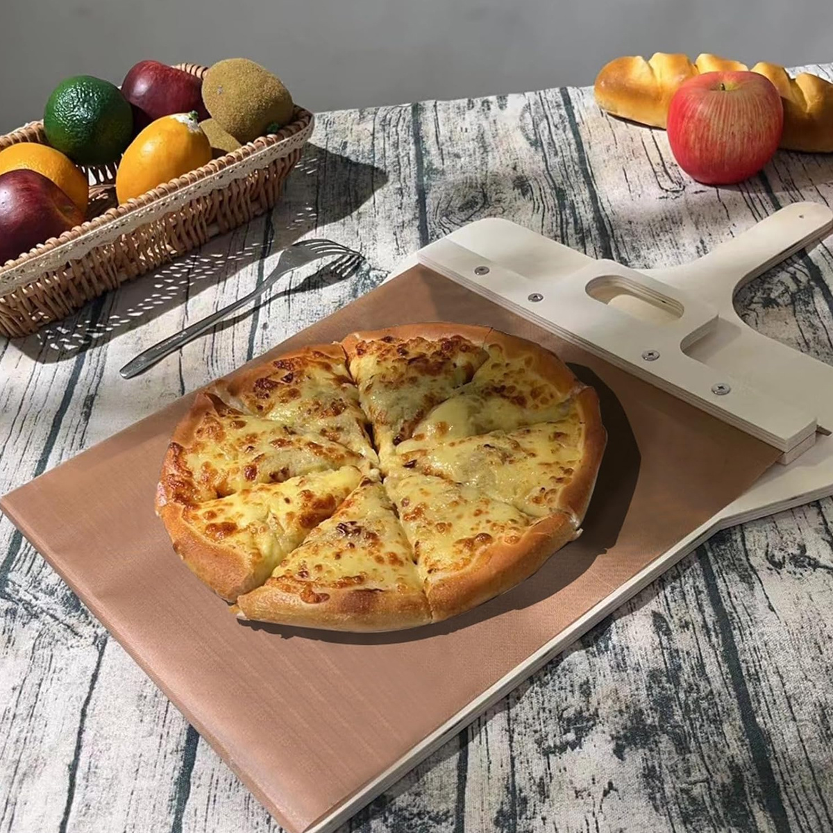 Eine geschnittene Pizza auf einem braunen Brett mit Obst und einer Gabel.