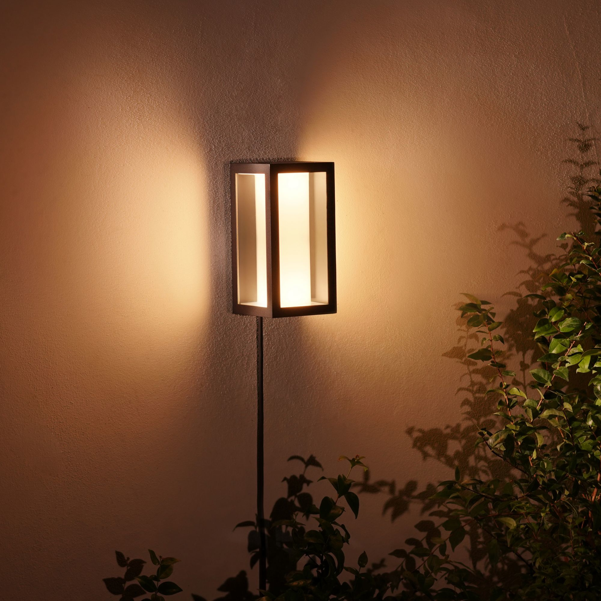 Außenwandleuchte an einer Wand. Licht scheint auf Wand und Blätter.