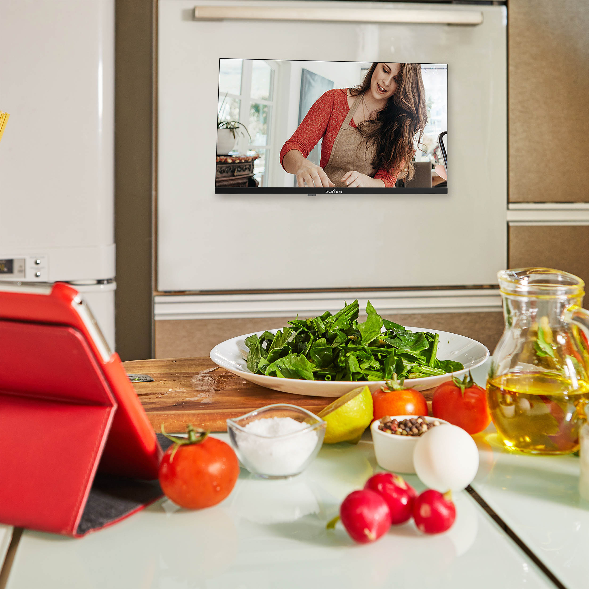 Eine Küchenszene mit Zutaten und einer Frau, die auf einem Fernsehbildschirm kocht. Ein Tablet ist auch sichtbar.