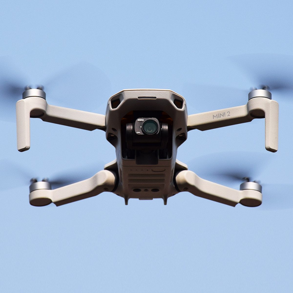 Drone in de lucht tegen een blauwe lucht. Het heeft vier armen met rotors en een camera.