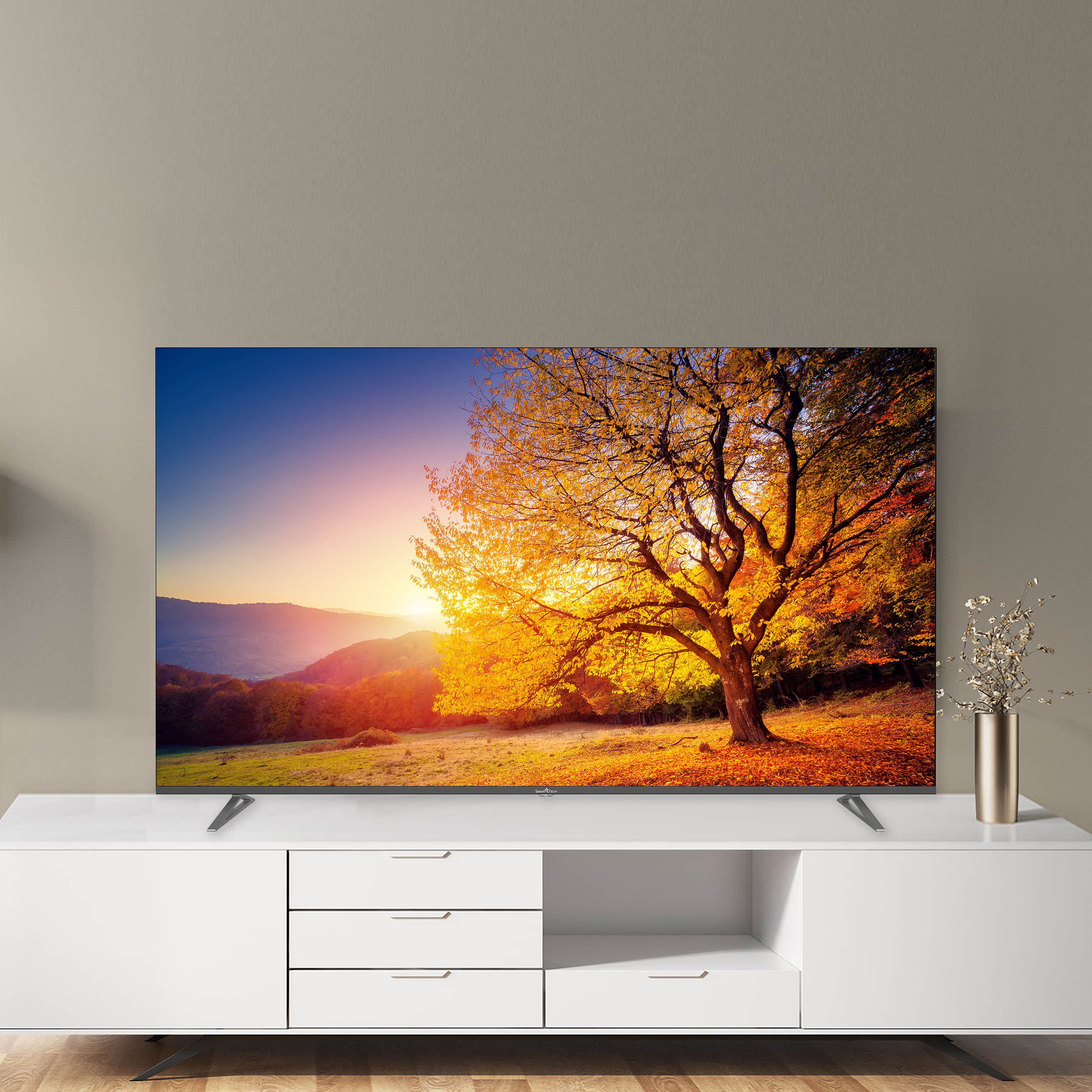 Telewizor wyświetla zachód słońca nad drzewem. Telewizor stoi na białej konsoli.