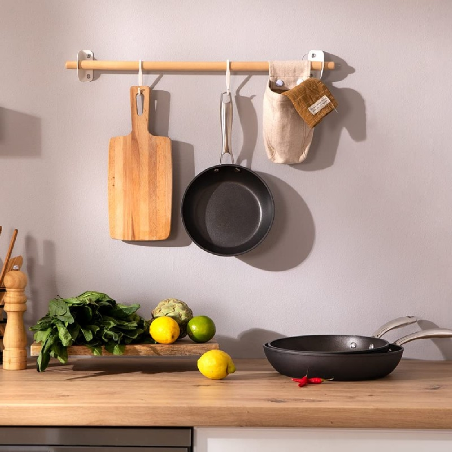 Keukenscène met houten snijplank, pan, groenten en citroenen. Een houten rail met items.