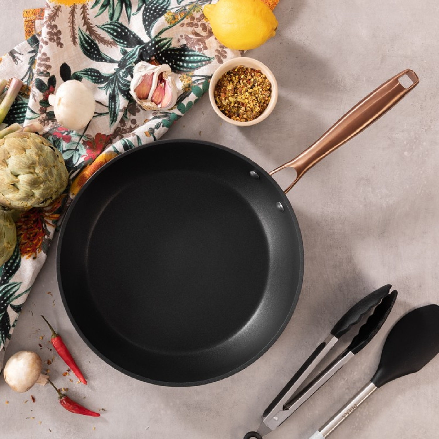 Widok z góry na patelnię ze składnikami i przyborami, w tym warzywami, ziołami i narzędziami.