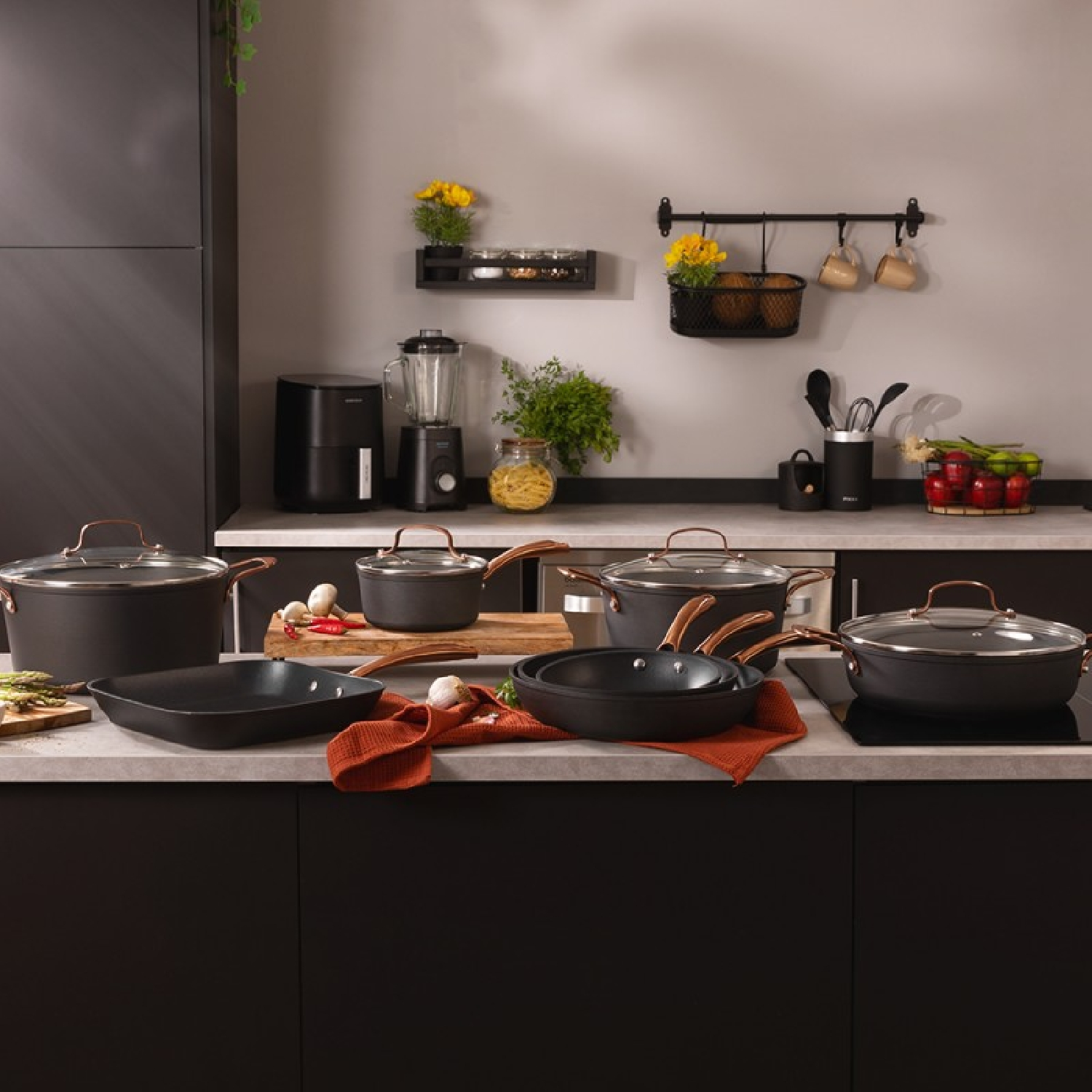 Scena kuchenna z czarnym zestawem naczyń, drewnianą deską do krojenia i różnymi elementami kuchennymi.
