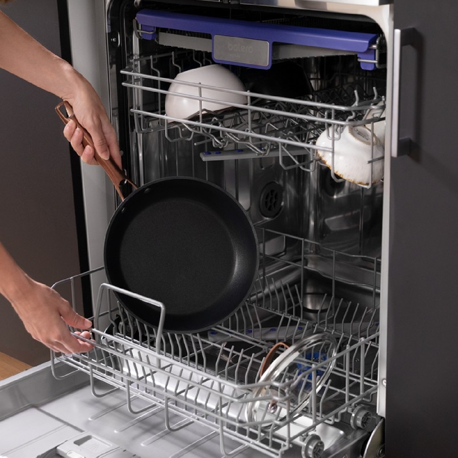 Osoba umieszczająca patelnię w zmywarce, widoczne są inne naczynia.
