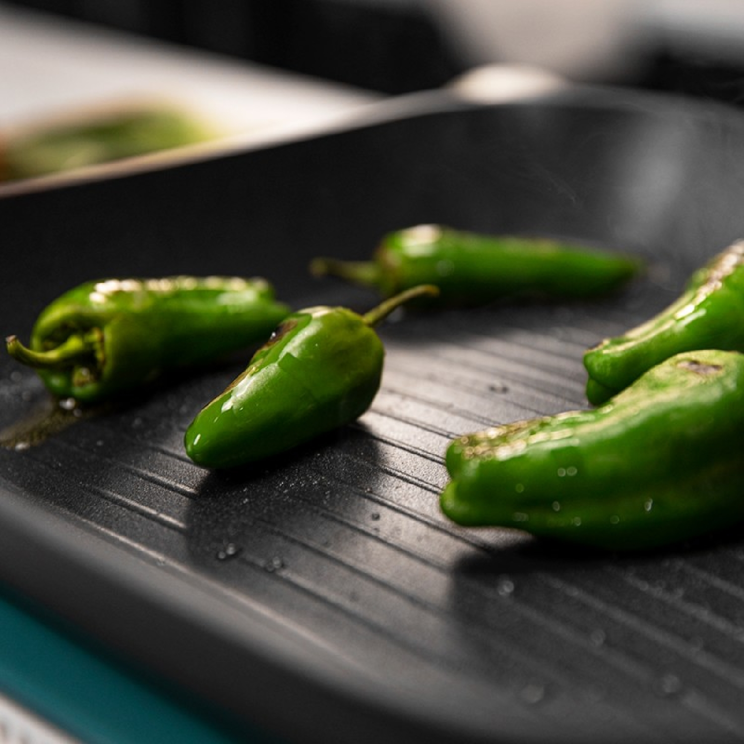 Pimientos verdes cocinándose en una sartén negra.