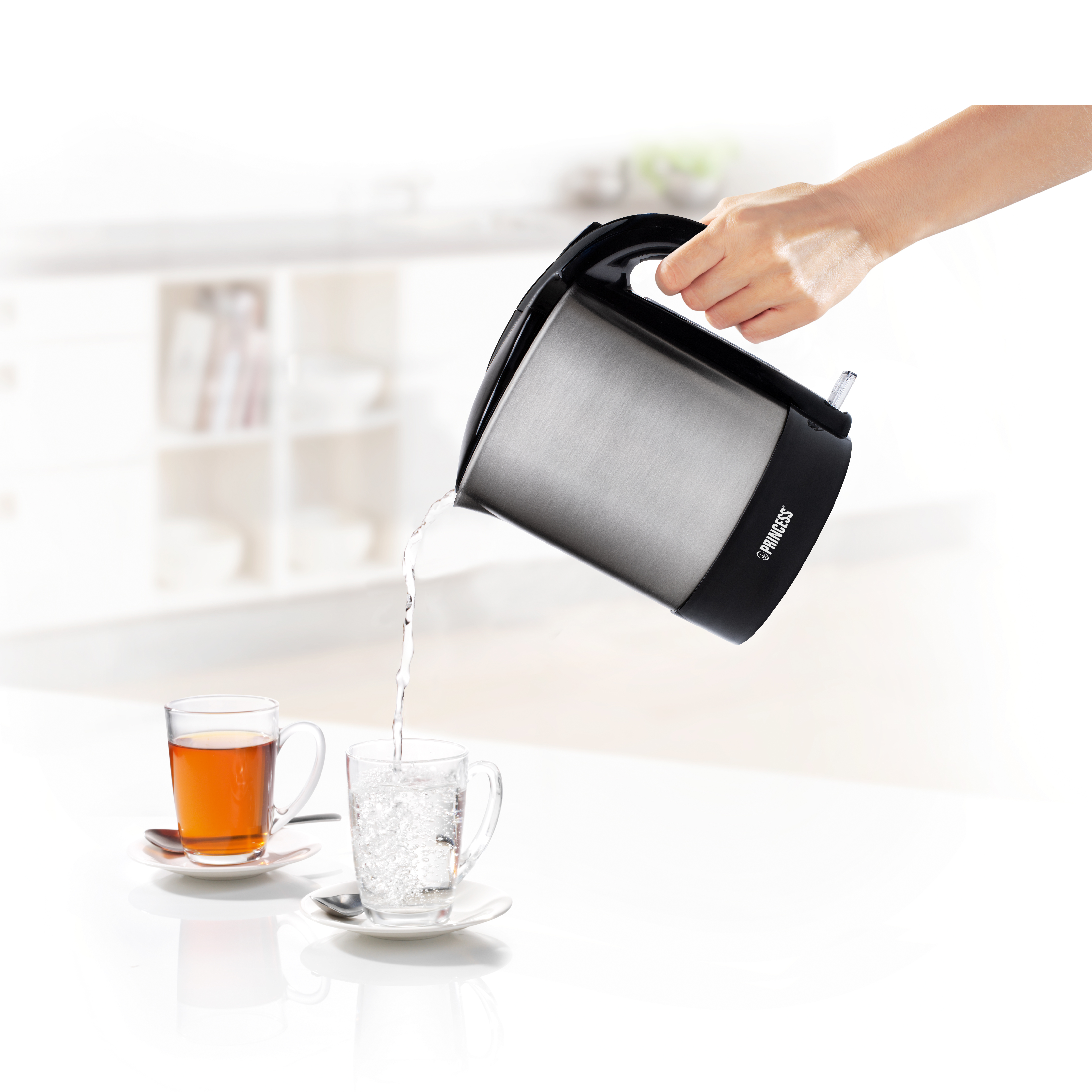 Ręka wlewa wodę ze stalowego czajnika do szklanki, obok szklanki herbaty.