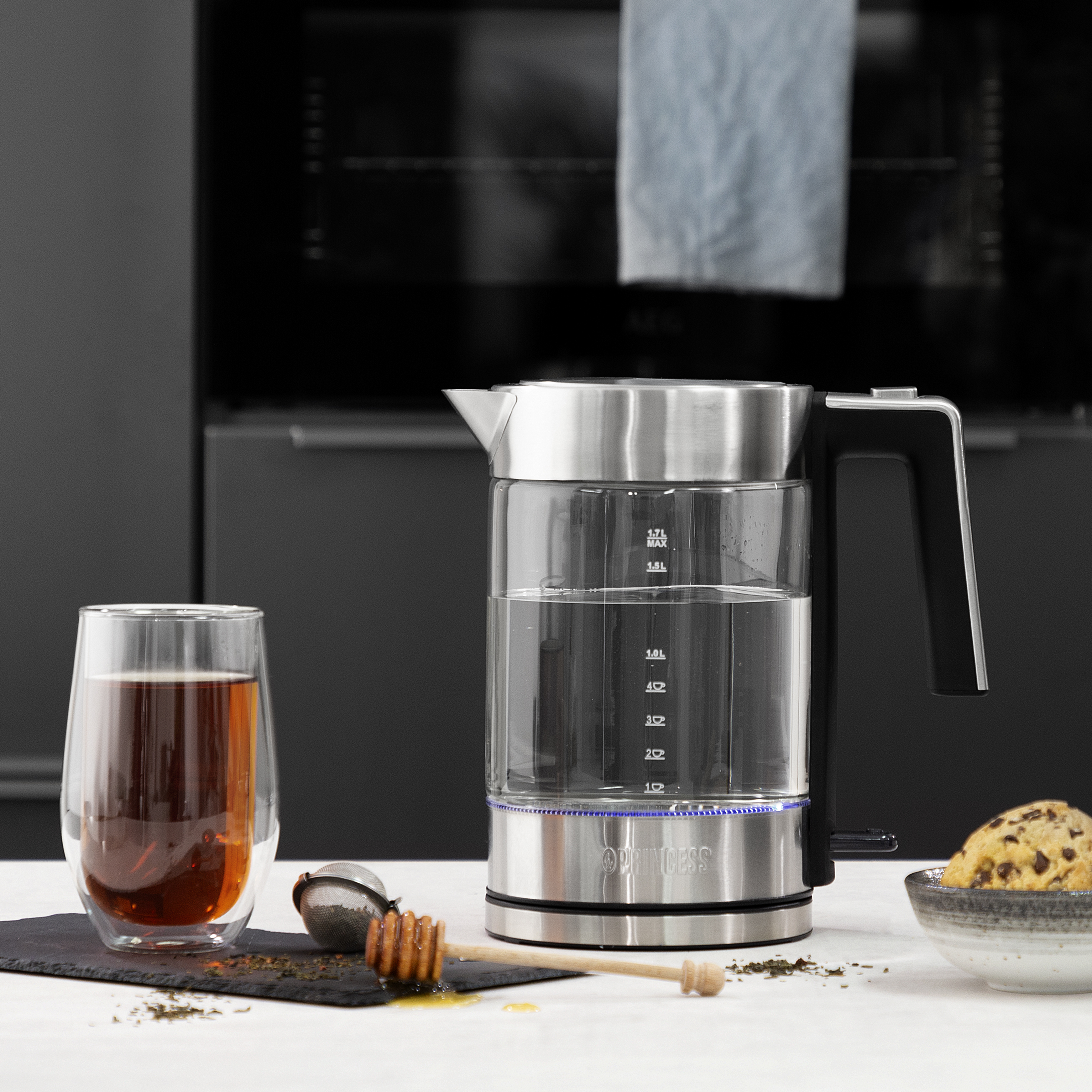 Ein transparenter Wasserkocher mit Wasser, neben einer Tasse Tee und Honig.