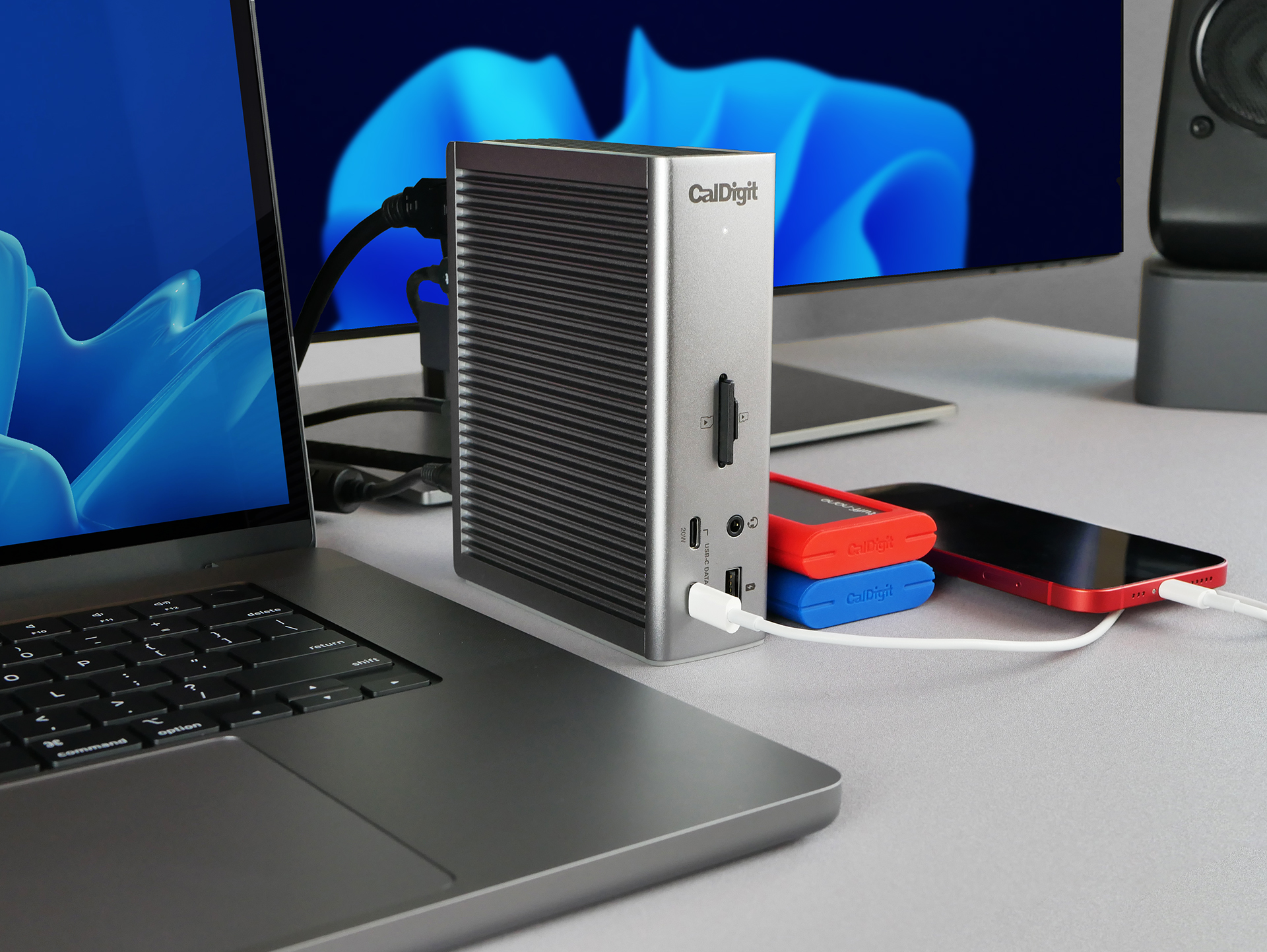 Docking station CalDigit argento collegata al laptop. Accessori rossi, blu e bianchi sulla scrivania.