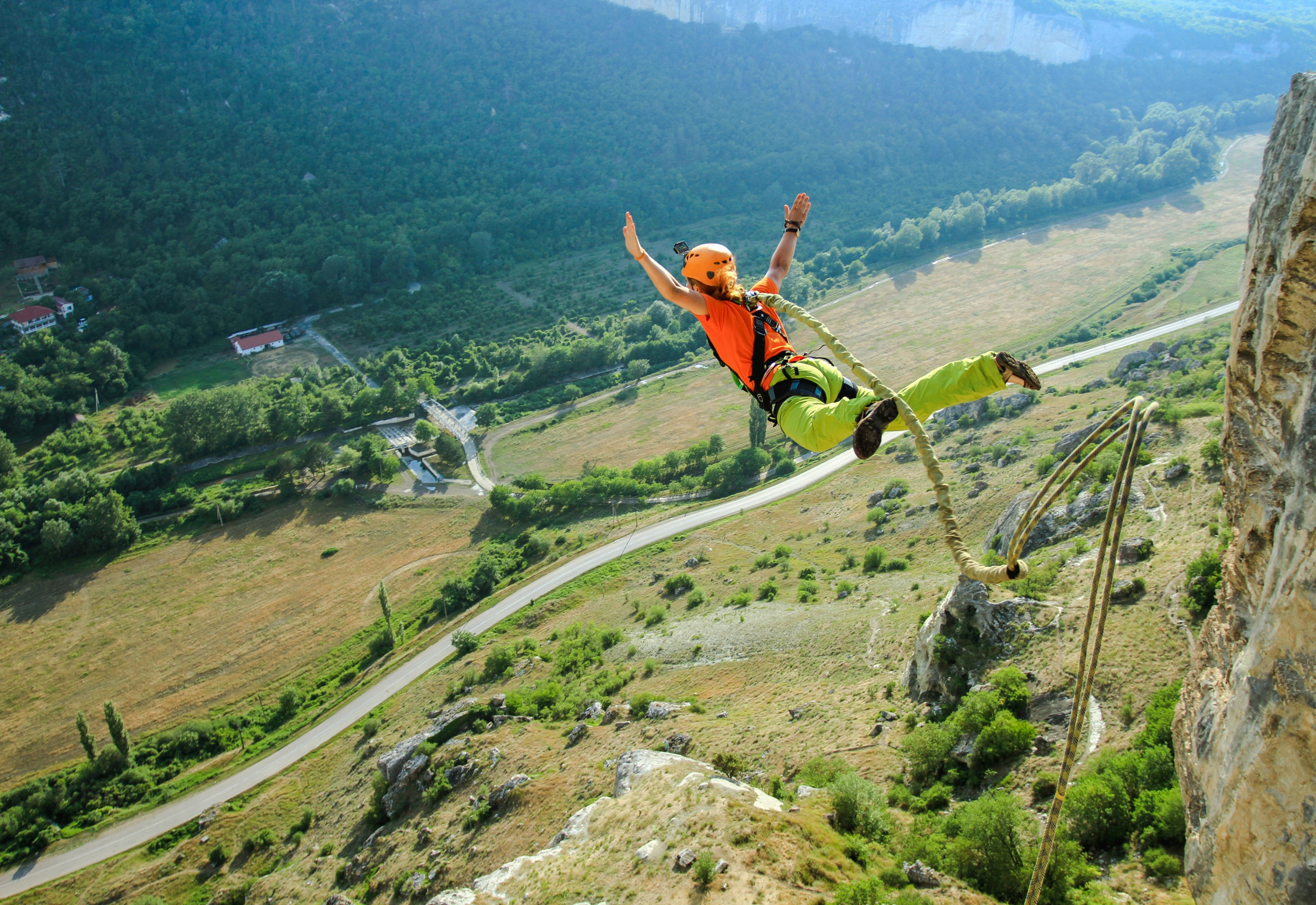 Person Bungee-Jumping von einer Klippe über einer grünen Landschaft.