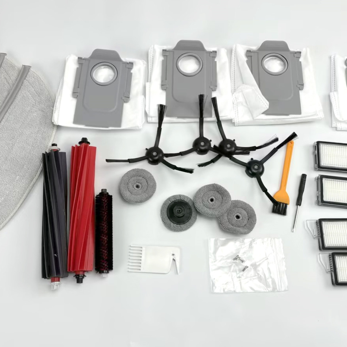 Części do odkurzacza: filtry, szczotki i worki ułożone na białej powierzchni.