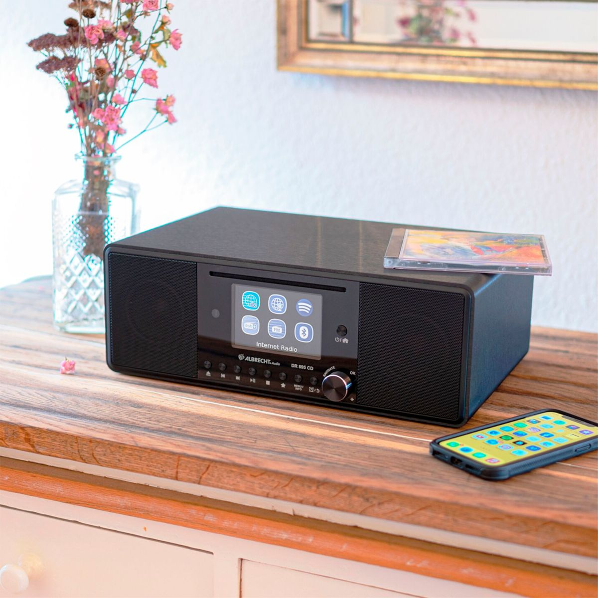 Czarny radio internetowe na drewnianym stole, z telefonem i płytą CD.
