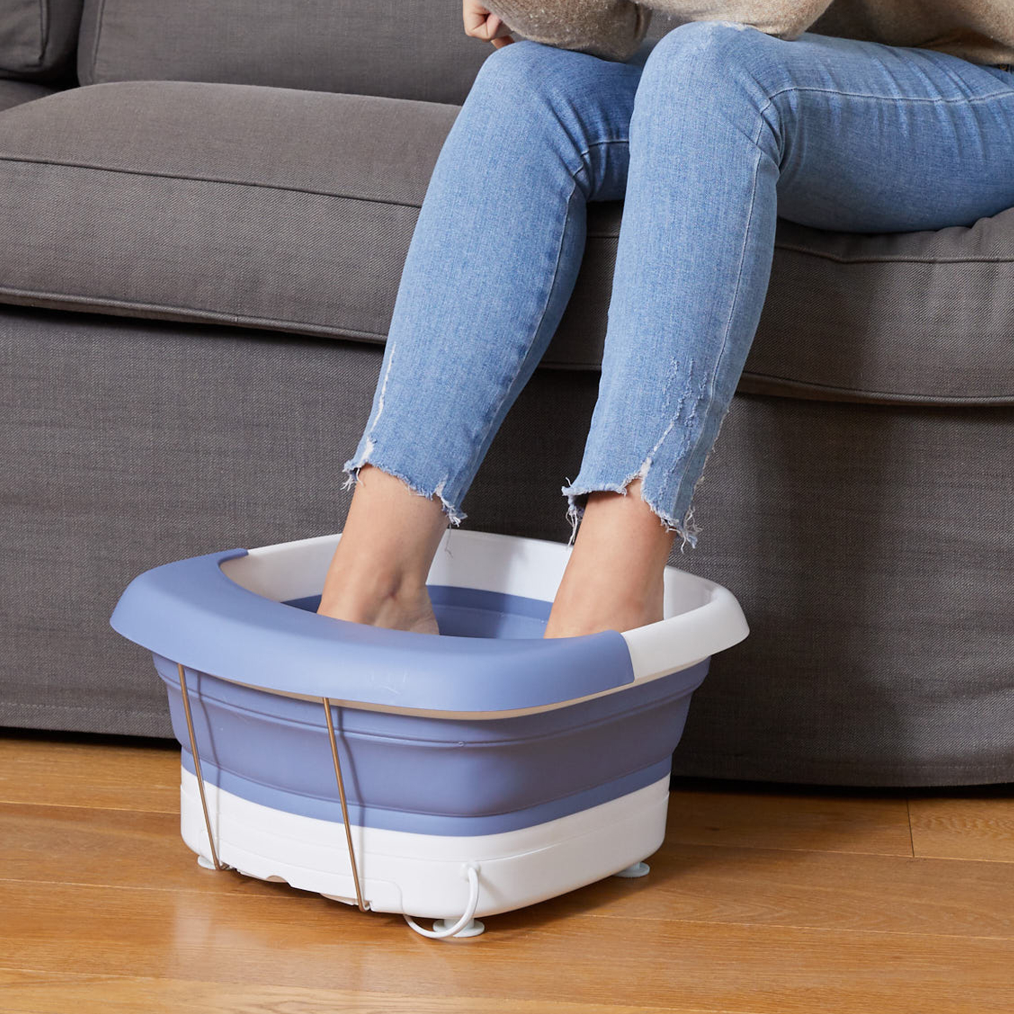 Feet in a blue and white foot spa, person sitting on a gray couch.