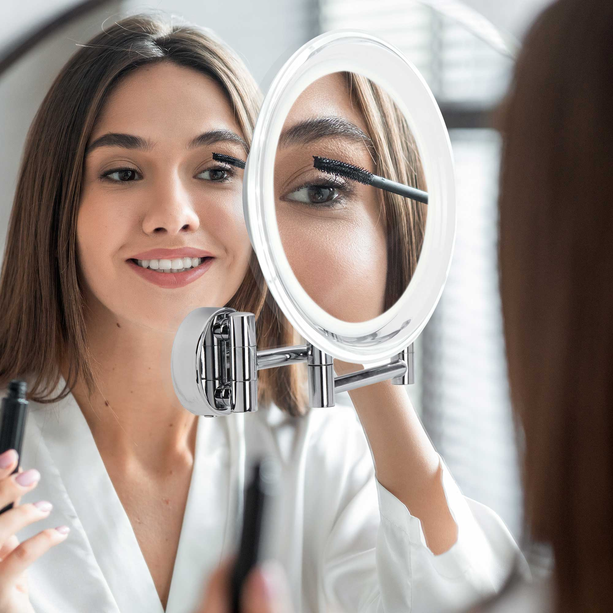 Frau, die Wimperntusche in einem beleuchteten Spiegel aufträgt.