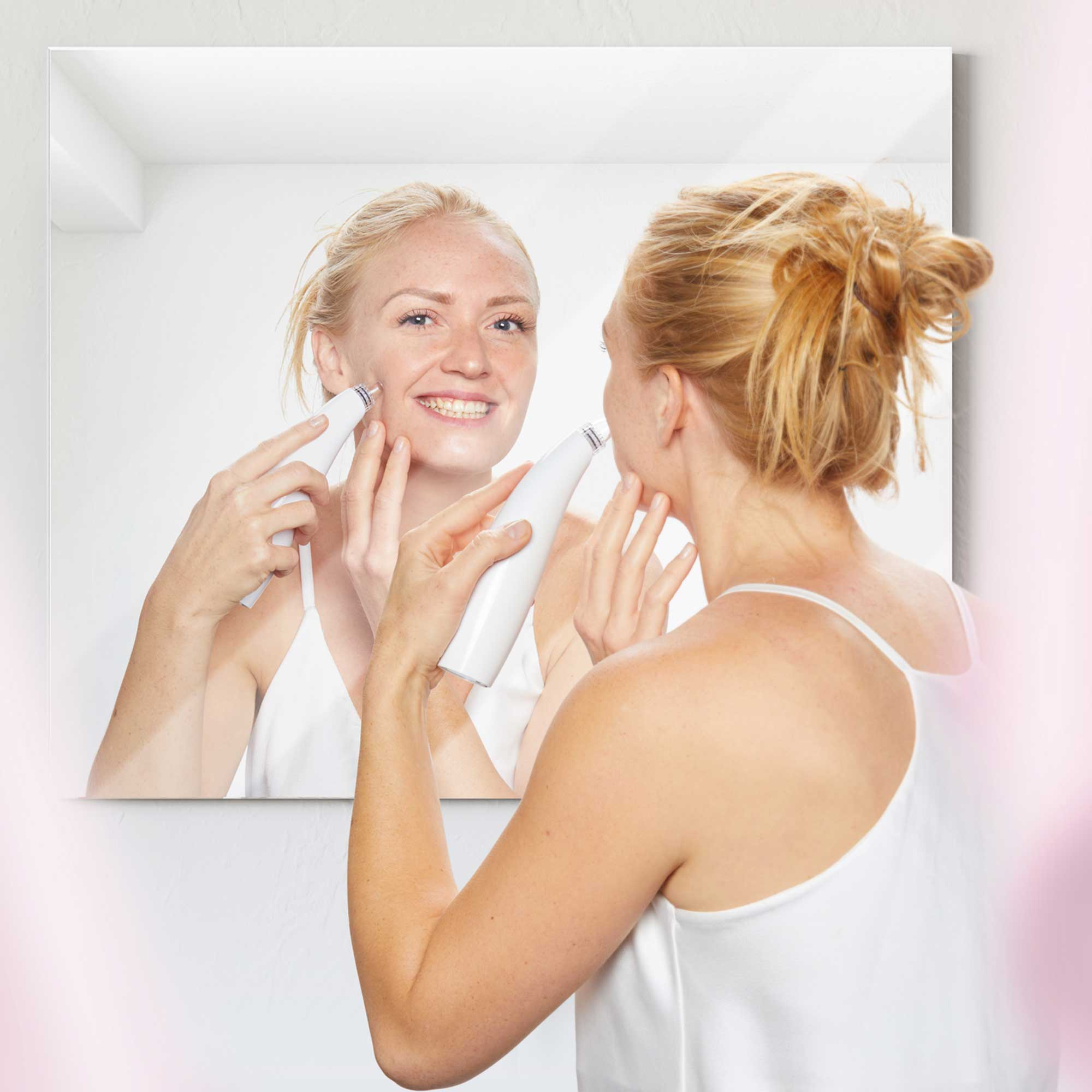 Woman using a facial cleaning device in front of a mirror, smiling.