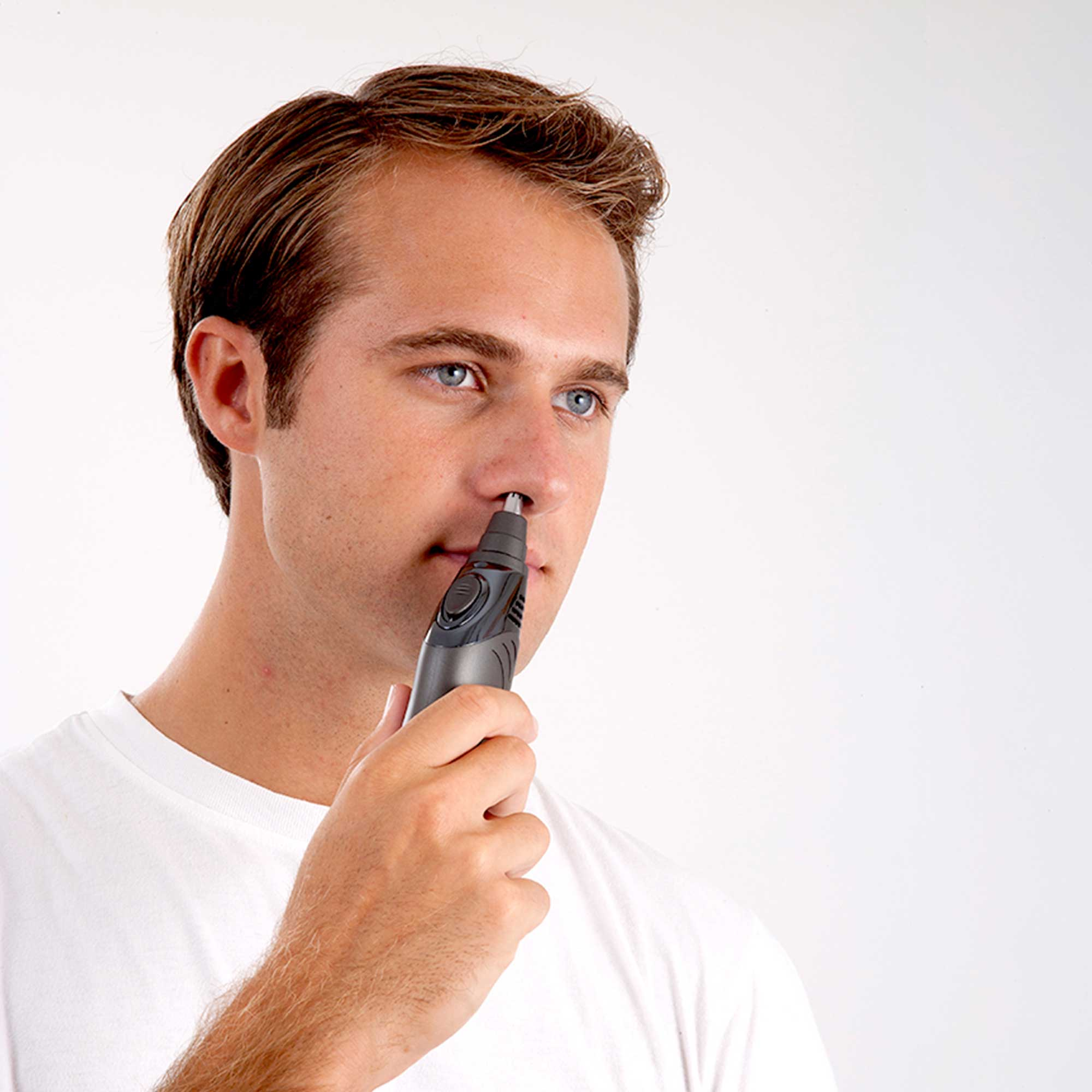 A man trims his nose hair with a black and gray trimmer. He's wearing a white t-shirt.