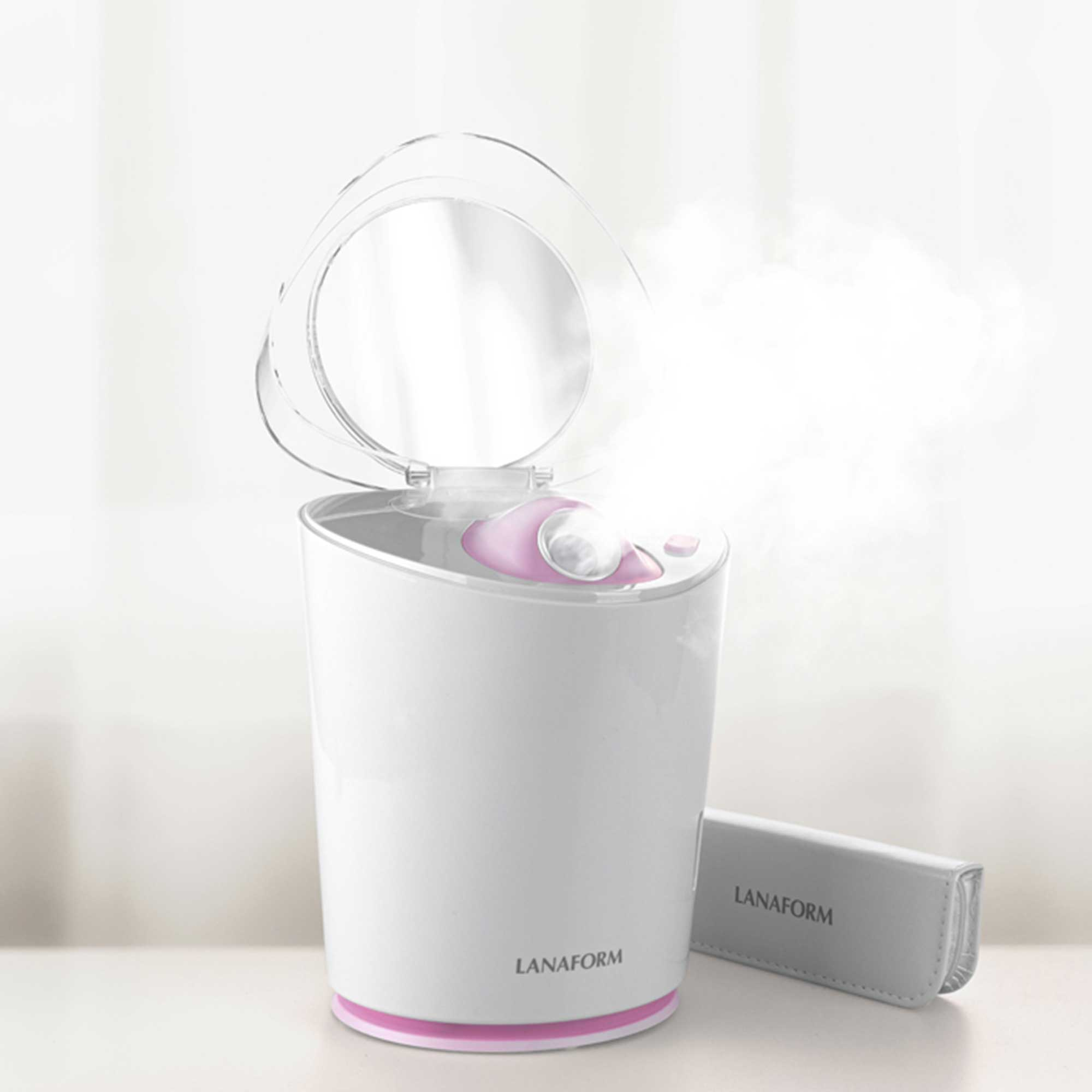 A white facial steamer with a clear lid, steam rising. A small accessory is at the side.