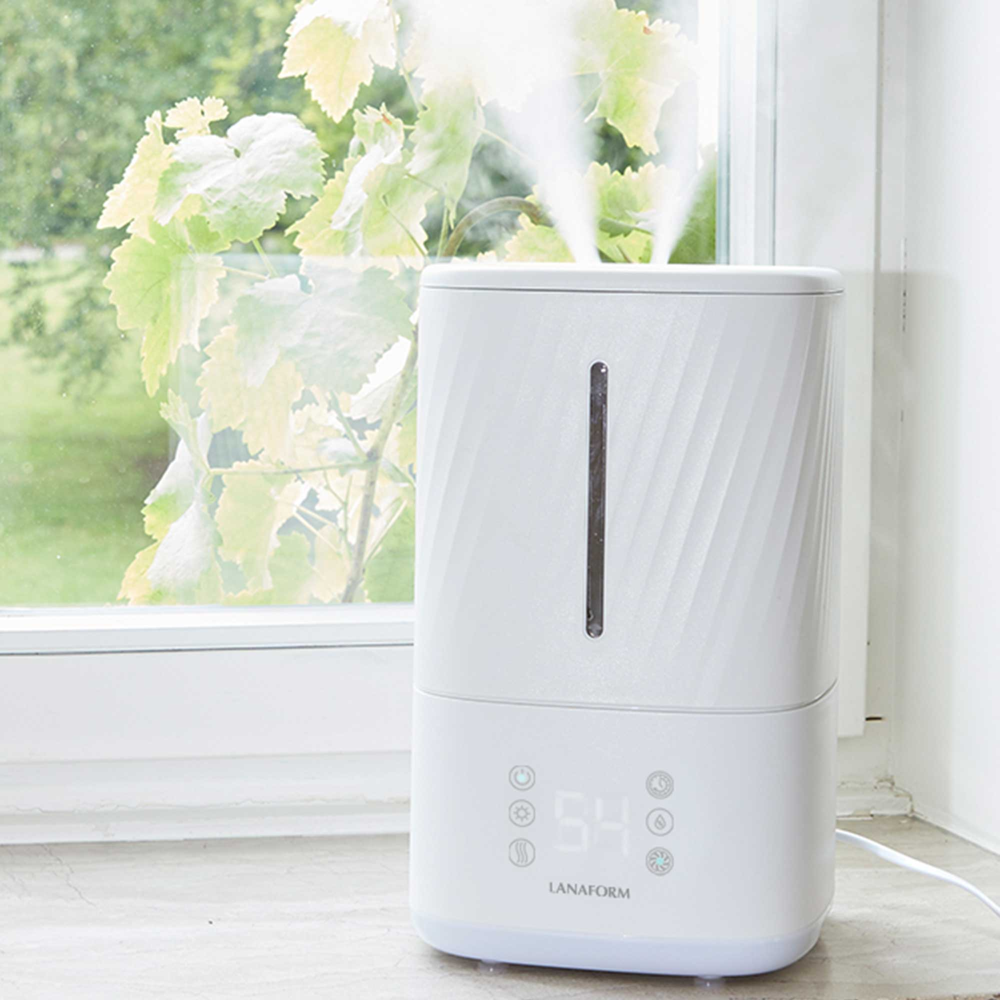 White humidifier on a window sill, mist visible, with a green leafy view outside.