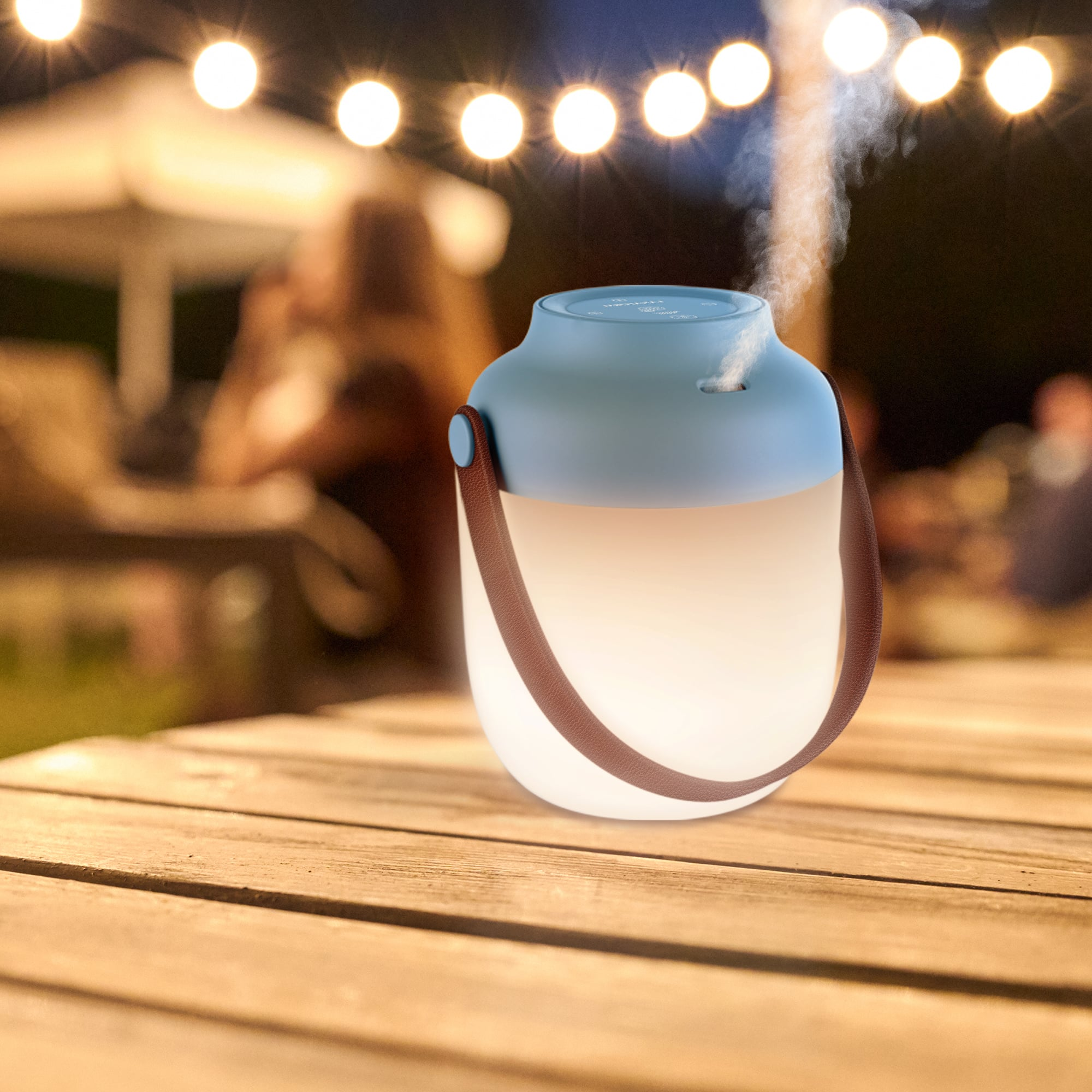 A blue and white lantern-shaped diffuser on a wooden table with lights in the background.