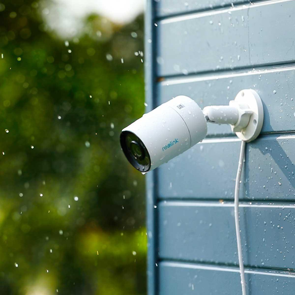 Biała kamera bezpieczeństwa zamontowana na niebieskiej ścianie, z kroplami wody w powietrzu.