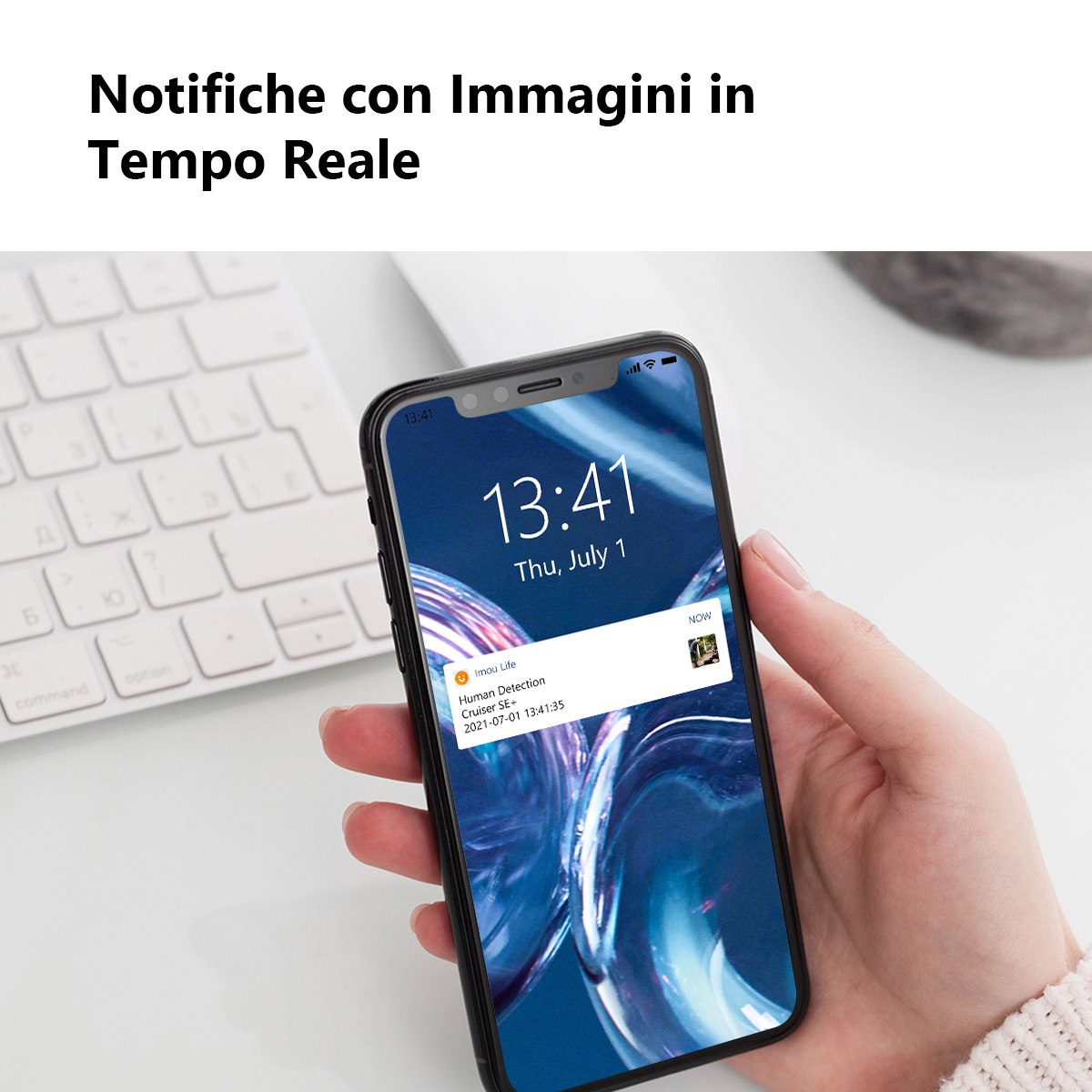 Dłoń trzymająca smartfon z powiadomieniem. Klawiatura widoczna w tle.