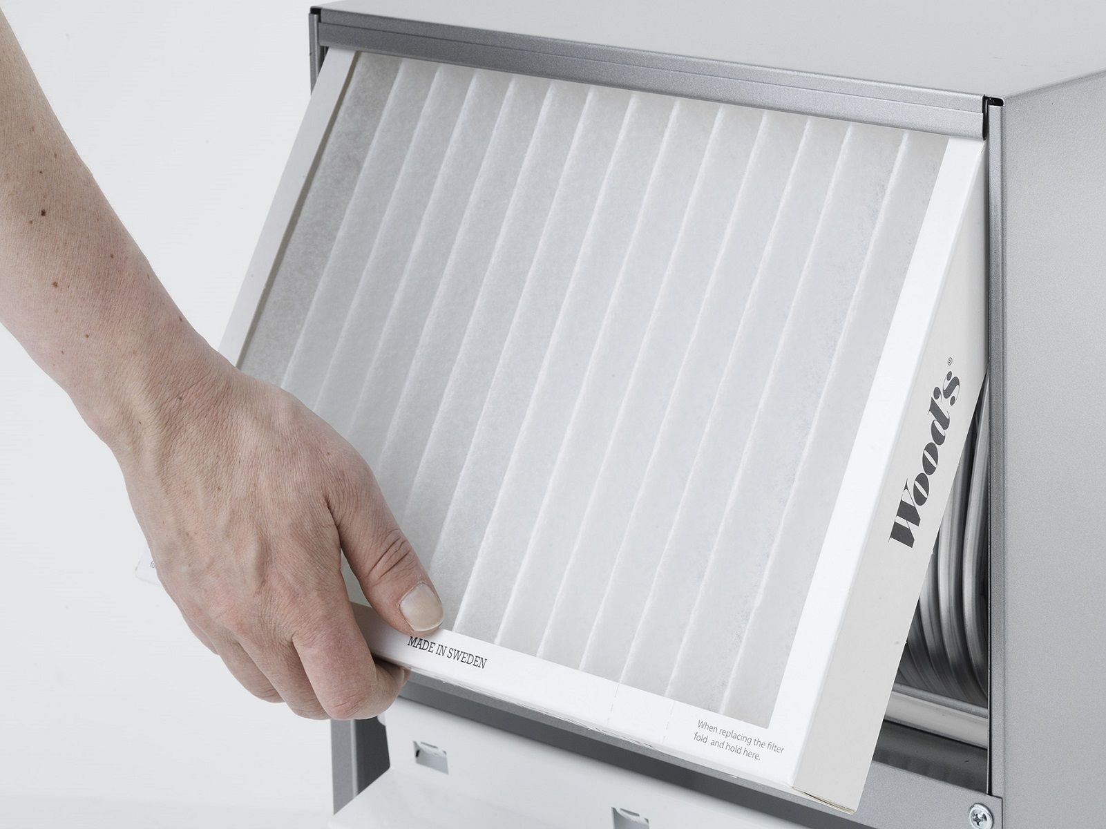 Eine Hand setzt einen weißen Filter in einen Metall-Luftreiniger ein.
