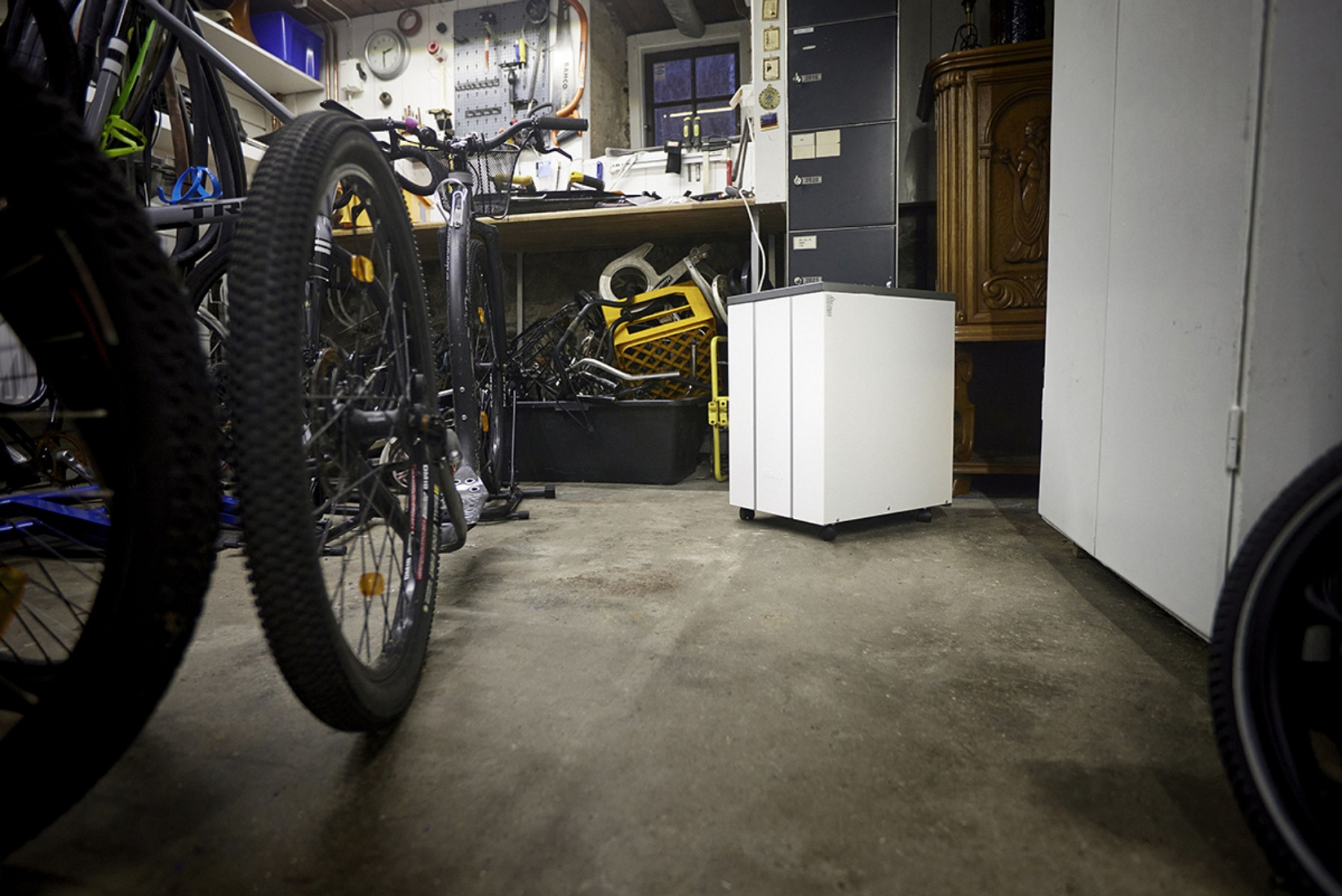 Garageninnenraum mit Fahrrädern, einer weißen Box auf Rädern und Werkzeugen an der Wand.