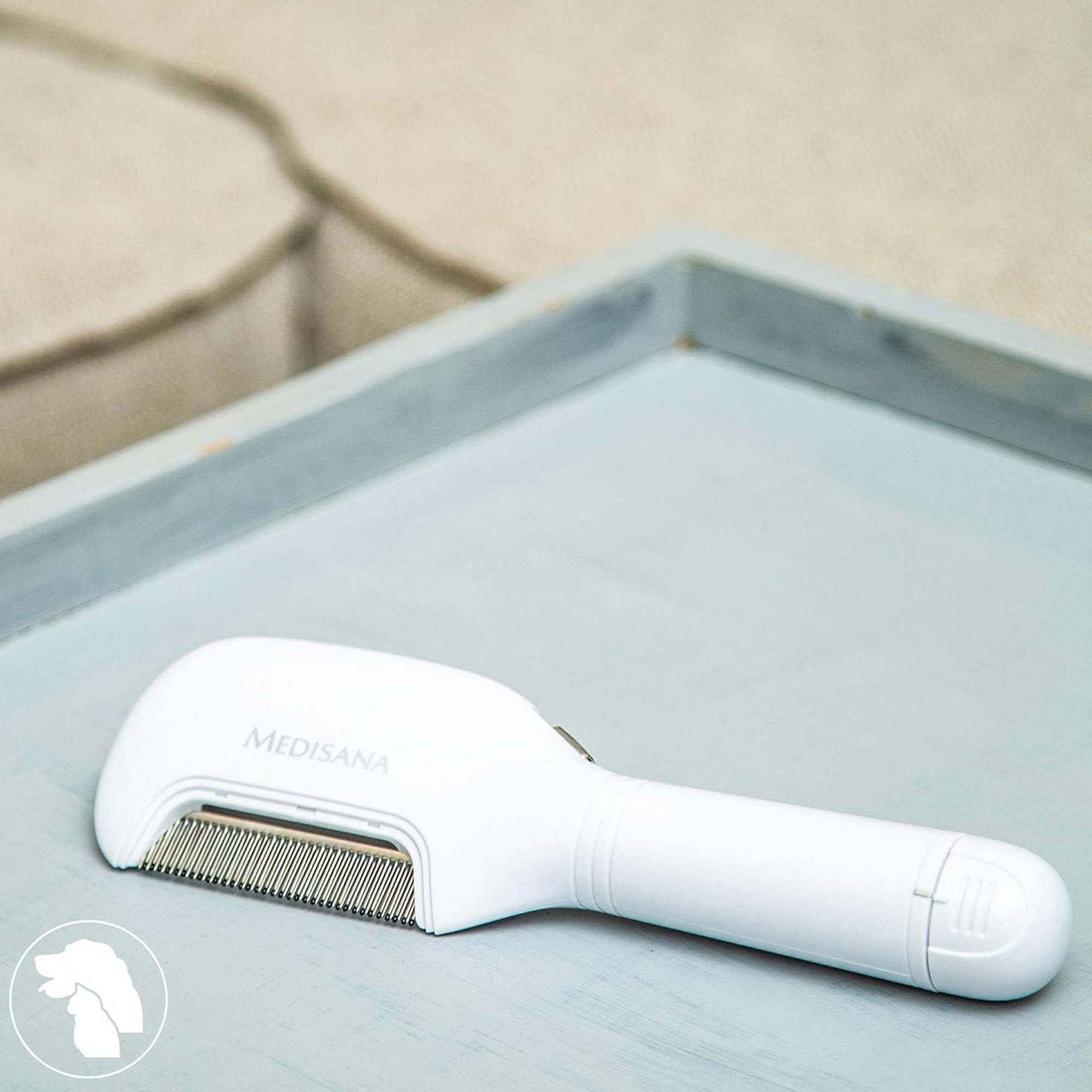 Un peigne blanc pour animaux de compagnie sur un plateau bleu-gris. Le peigne a des dents métalliques et la marque est visible.