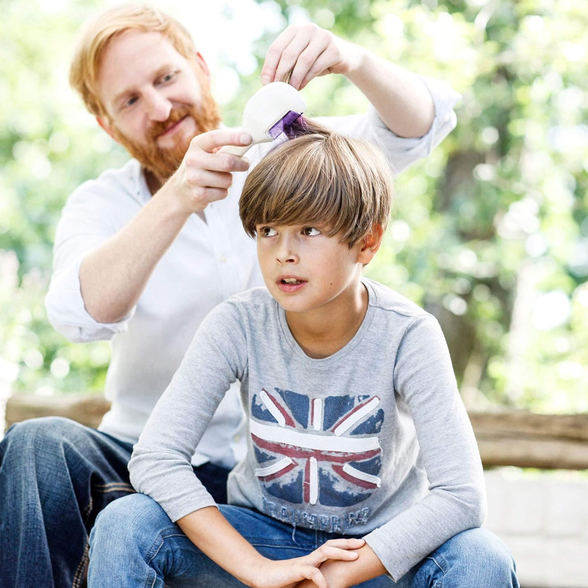 Un père coiffe les cheveux de son fils à l'extérieur. Le fils regarde en haut.