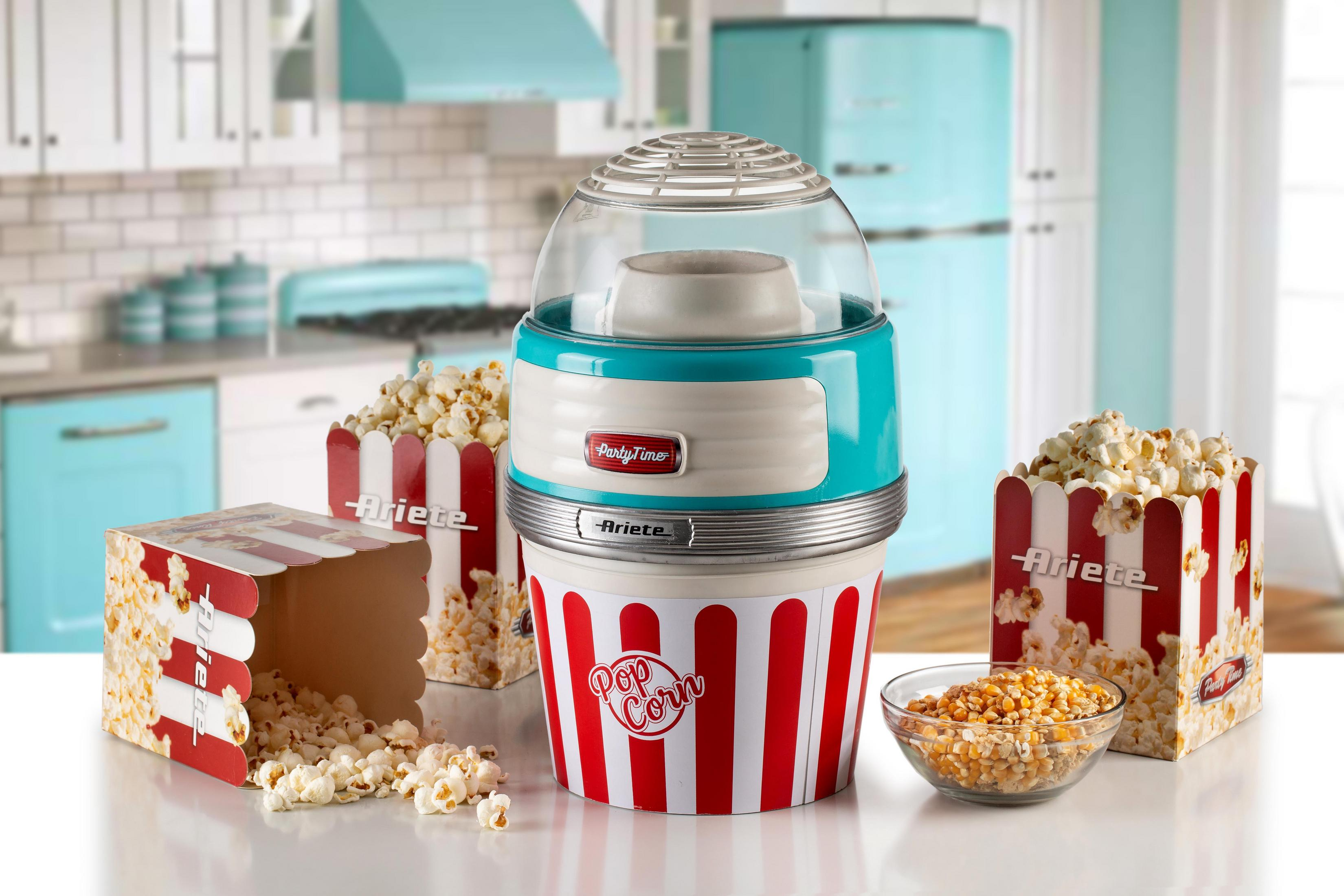Eine Popcornmaschine mit rot-weißen Popcornboxen und einer Schüssel mit Maiskörnern auf einer weißen Oberfläche.