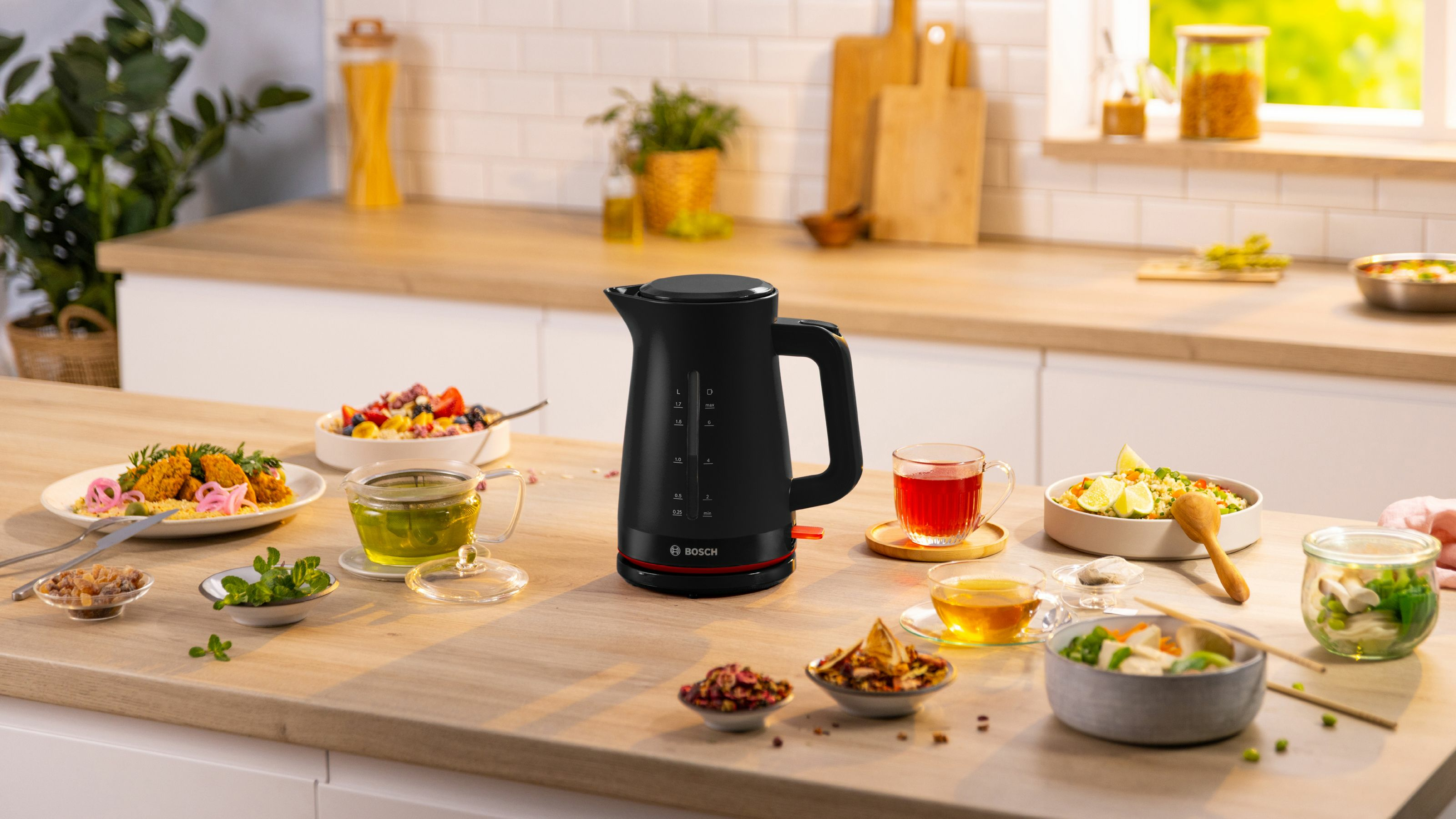 Zwarte elektrische waterkoker met voedselarrangement. Diverse kleine kommen met eten op houten tafel.