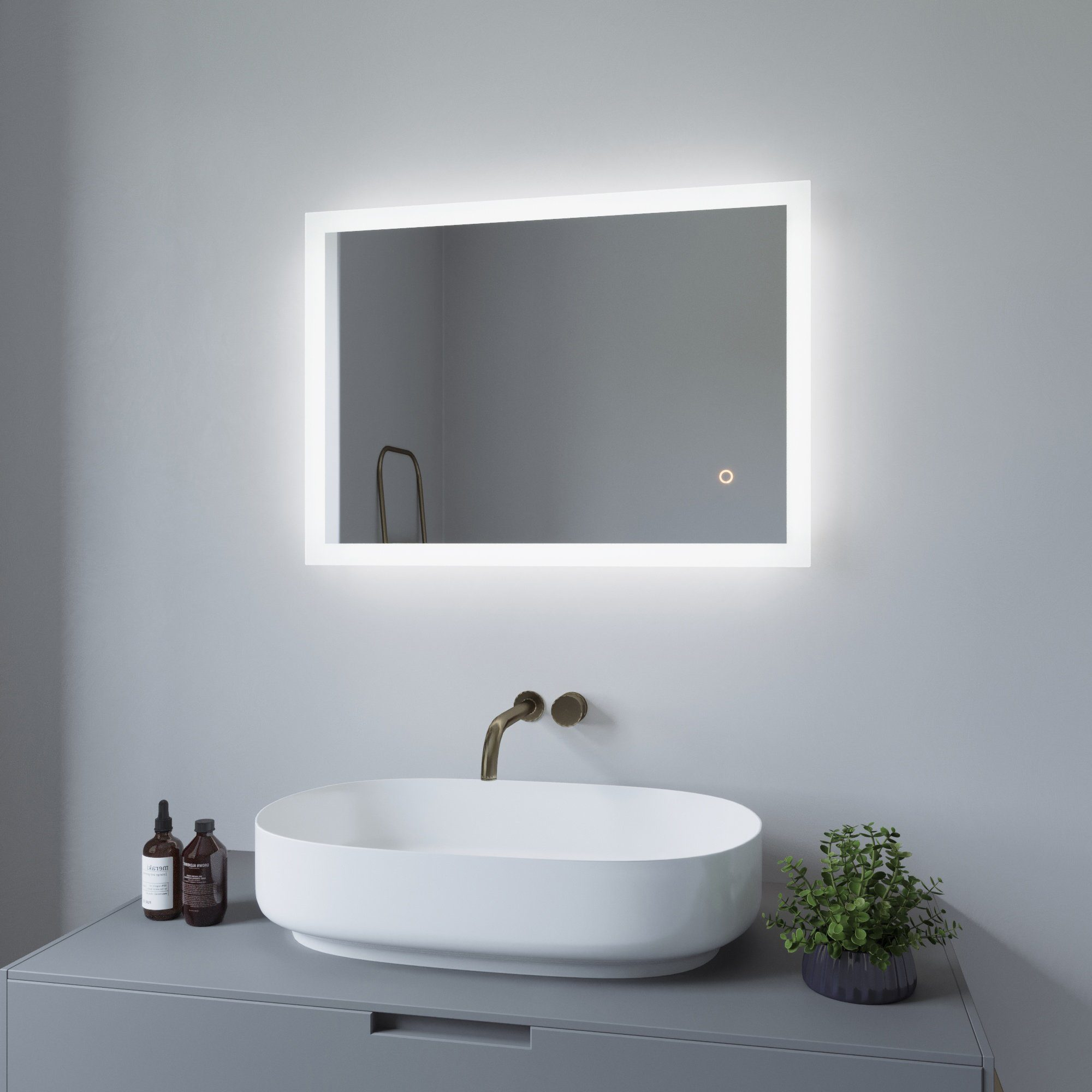 Badezimmer mit Spiegel über Waschbecken, Pflanze und Flaschen auf der Ablage.