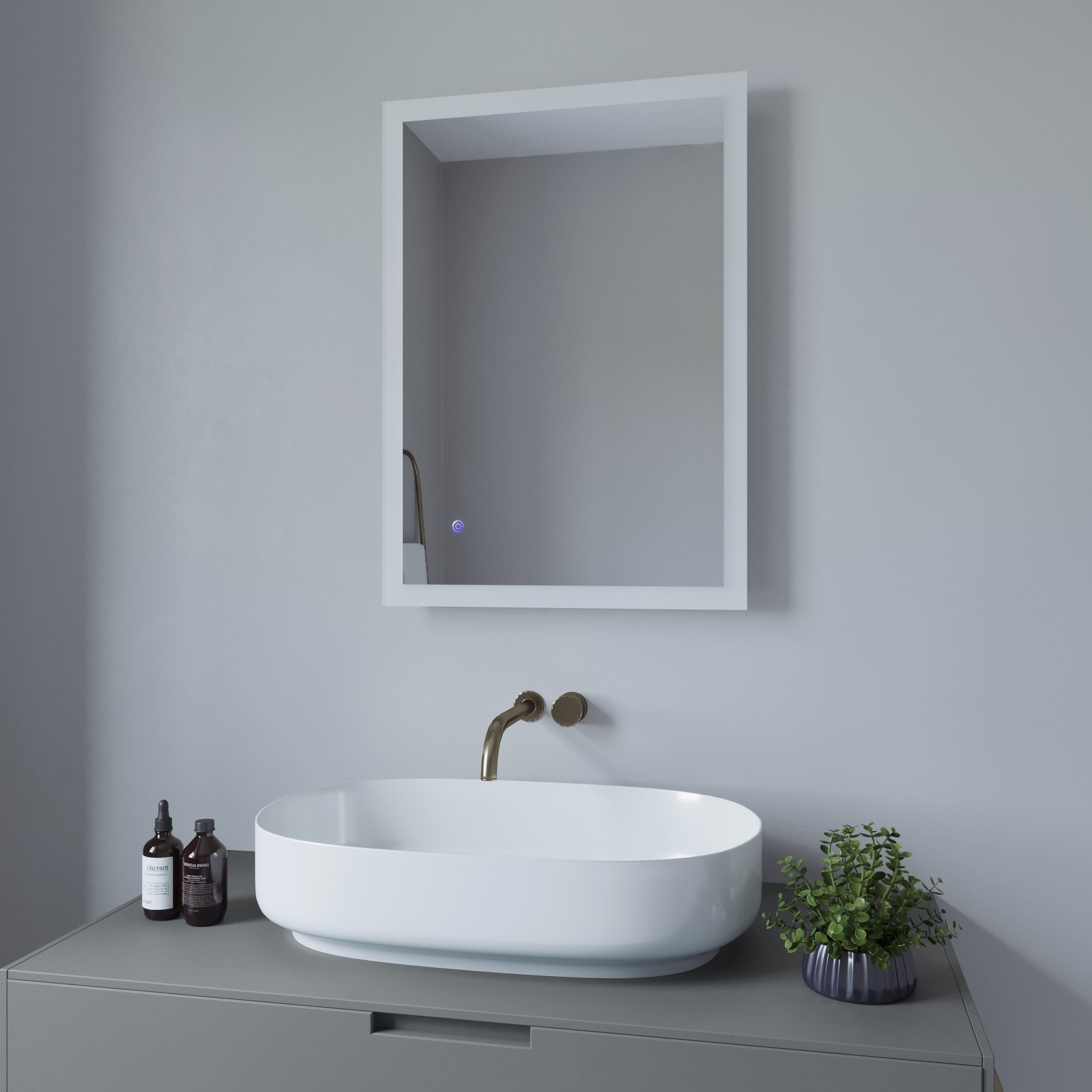 Badezimmer mit Spiegel, Waschbecken und Wasserhahn. Flaschen und eine Pflanze stehen auf der Theke.
