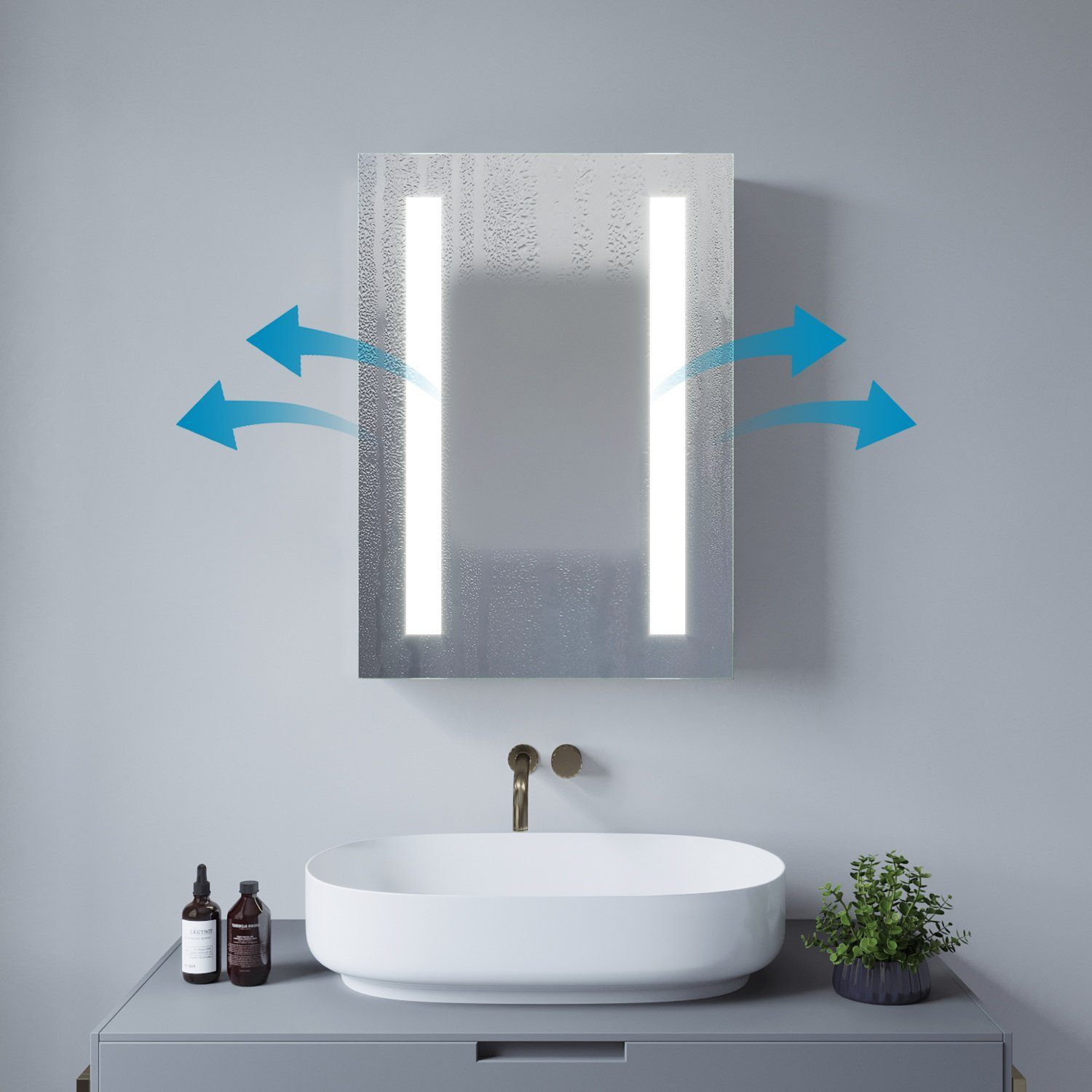 Ein Spiegel mit zwei vertikalen Lichtern und blauen Pfeilen. Ein weißes Waschbecken, Flaschen und eine Pflanze darunter.