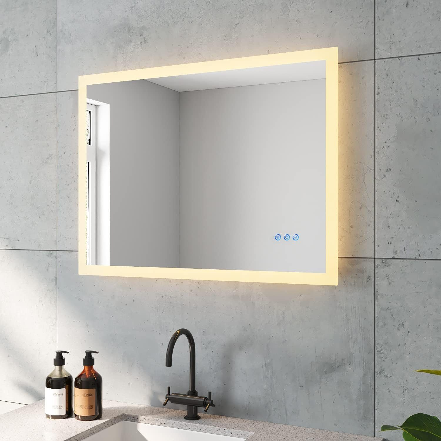 Ein rechteckiger, hintergrundbeleuchteter Spiegel ist an einer gefliesten Wand befestigt. Unter dem Spiegel befinden sich ein Wasserhahn und ein Waschbecken.