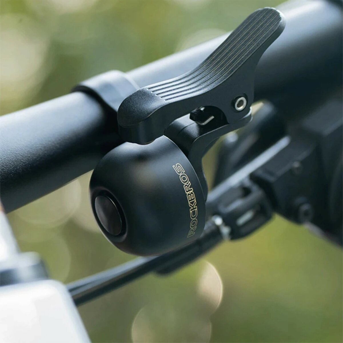 Czarny dzwonek rowerowy zamontowany na kierownicy, z widocznym logo Rockbros. Zbliżenie.