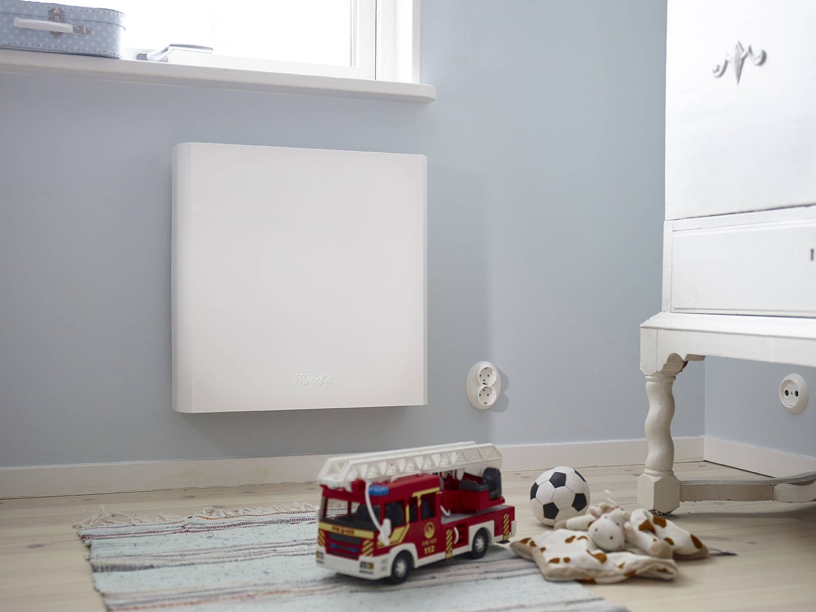 Weißer Wandheizkörper an einer blauen Wand in einem Kinderzimmer. Enthält einen Spielzeug-Feuerwehrwagen und anderes Spielzeug auf dem Boden.