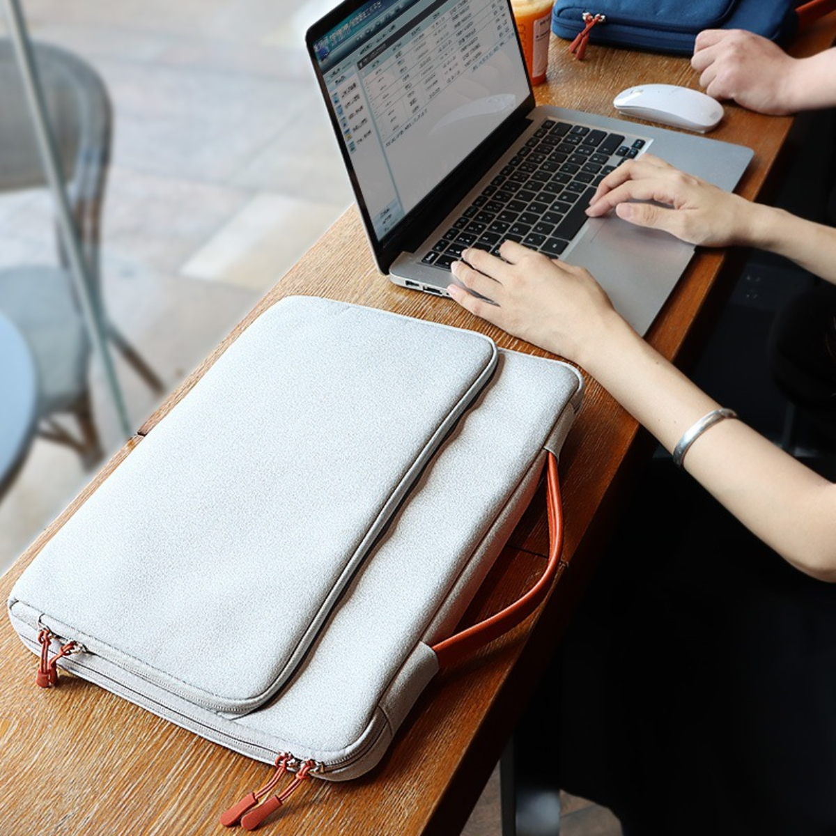 Person nutzt Laptop auf Tisch, mit Laptoptasche. Arm einer anderen Person sichtbar.