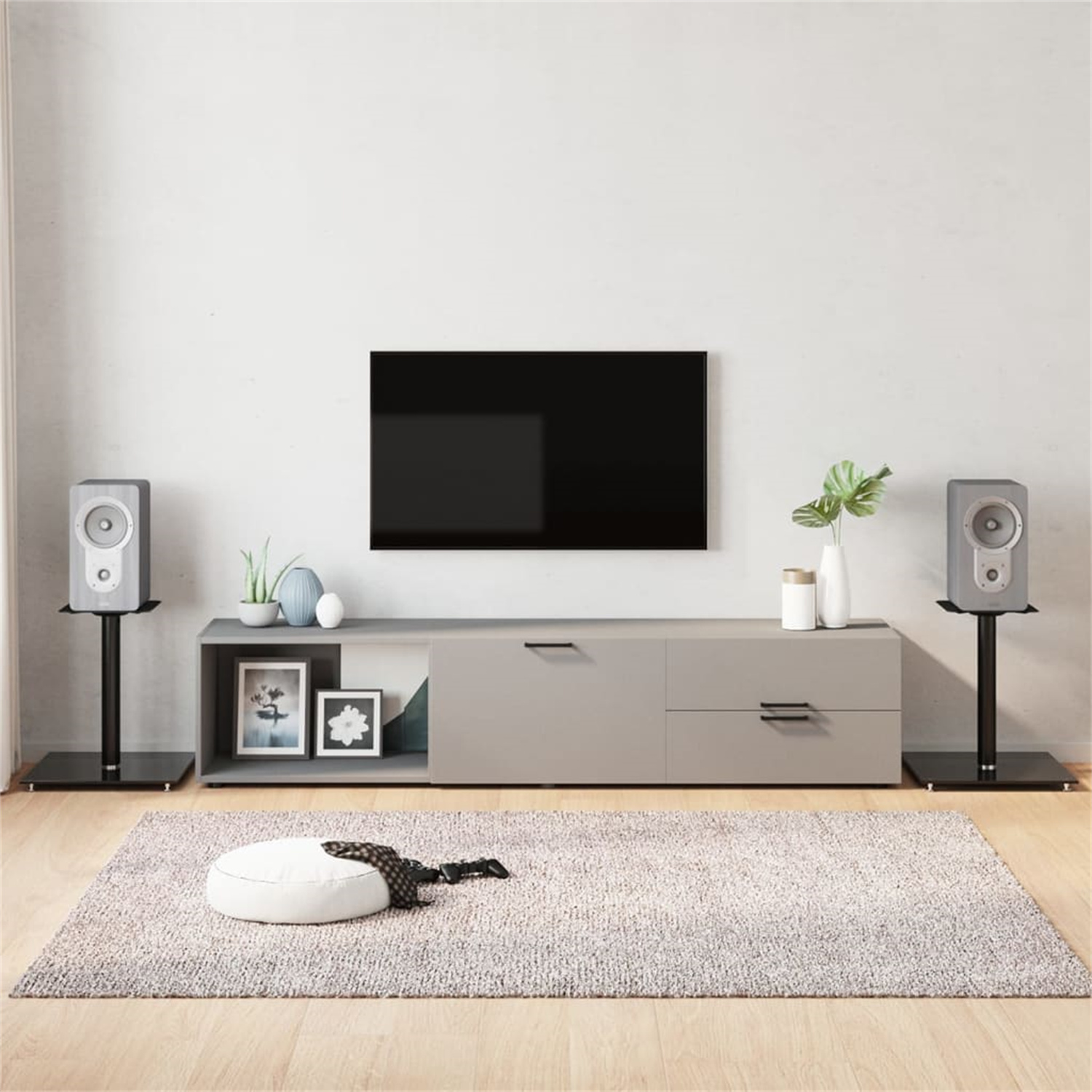 Wohnzimmer mit Fernseher, Lautsprechern und Teppich. Der Fernseher steht über einem langen Schrank. Lautsprecher auf Ständern.