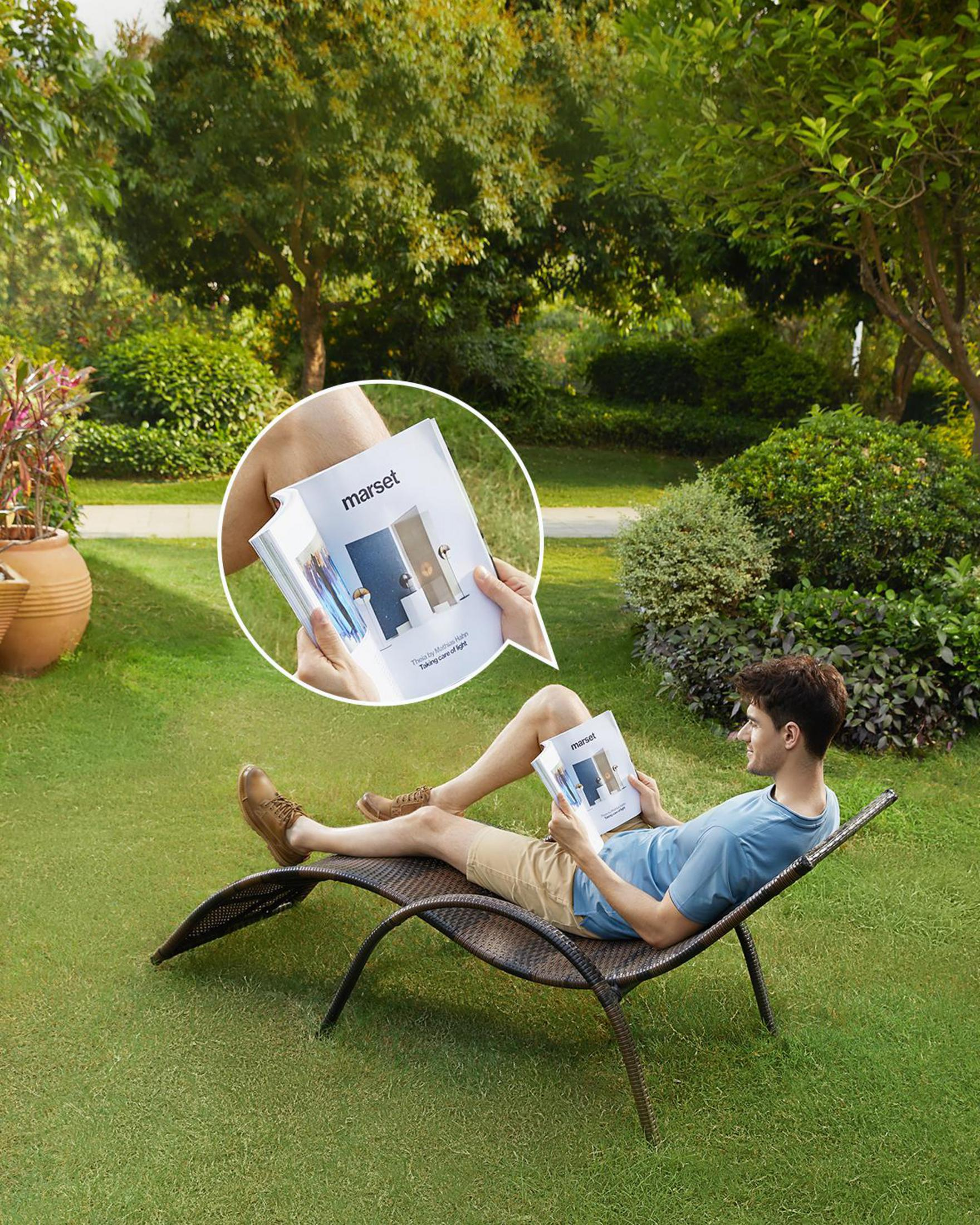 Mężczyzna relaksuje się na leżaku w ogrodzie, czytając książkę.