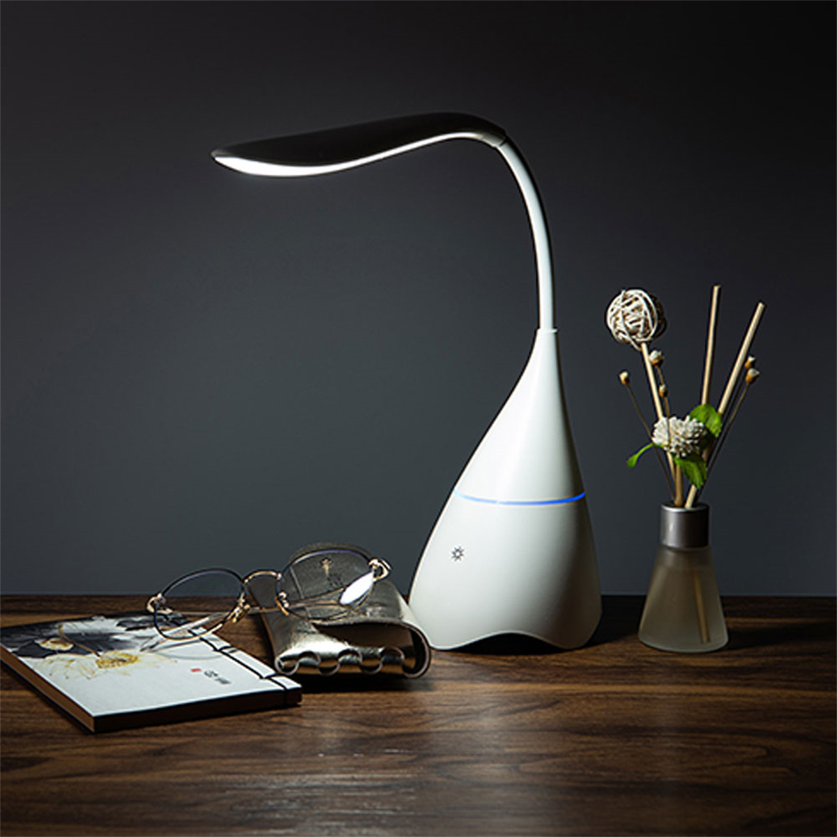 Weiße Schreibtischlampe, Brille, Buch und Vase mit Blumen auf einem Holztisch.