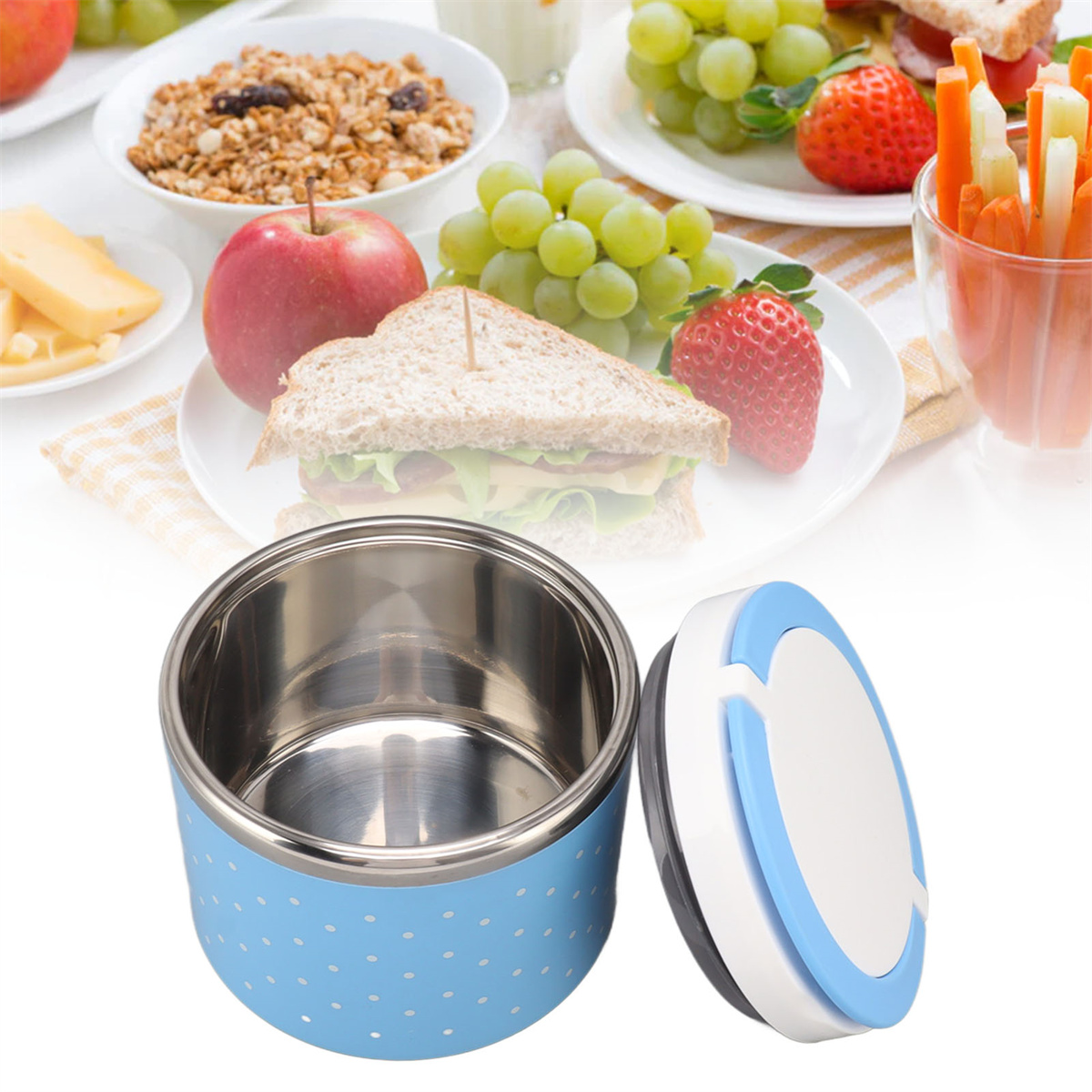 Eine blaue Lunchbox mit Polka Dots, geöffnet, mit Brot, Obst und Gemüse im Hintergrund.