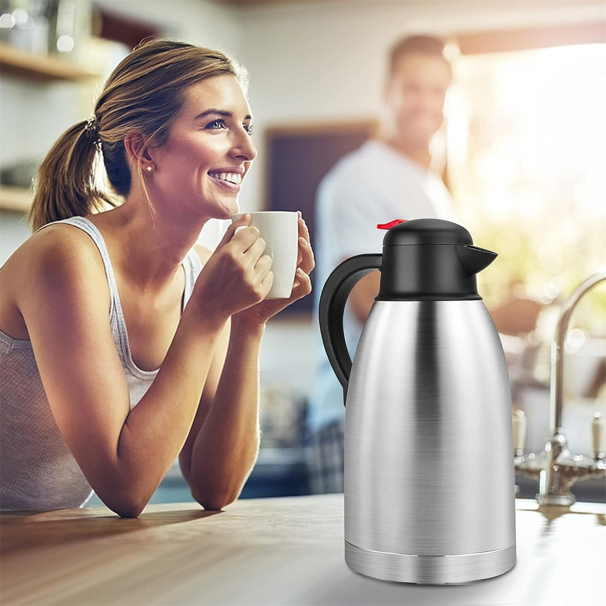 Lächelnde Frau hält weißen Becher, neben silberner Thermoskanne auf Holztheke. Mann im Hintergrund.