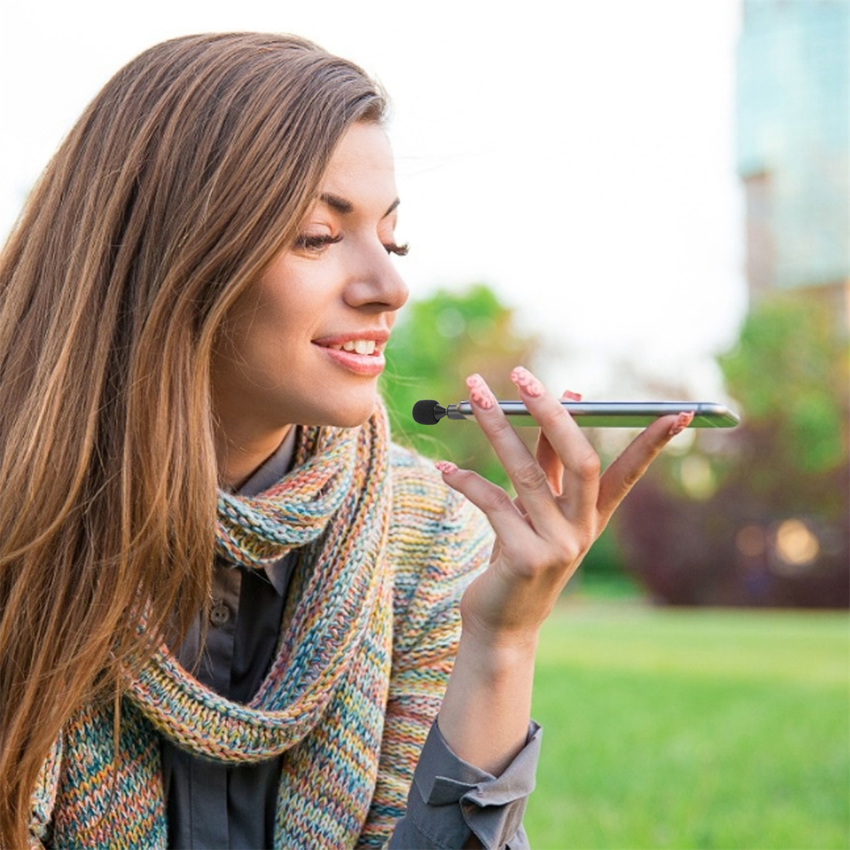 Eine Frau, die ein Telefon mit Mikrofon hält, im Freien in einem Park.