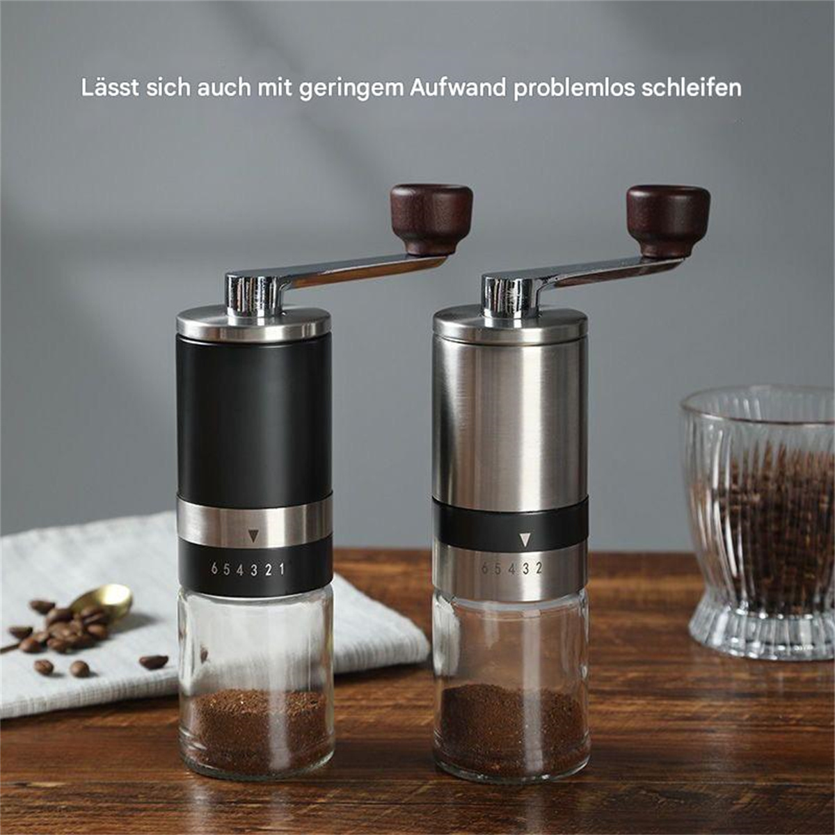 Zwei manuelle Kaffeemühlen mit Holzgriffen und Gläsern. Ein Löffel und Kaffeebohnen sind in der Nähe.
