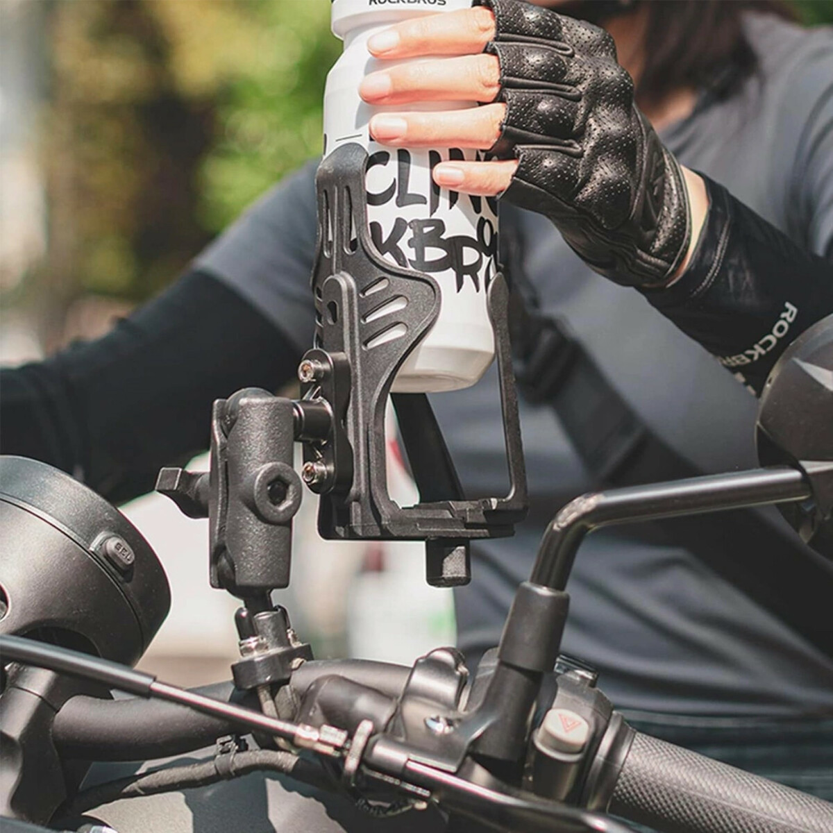 Een persoon die een waterfles vasthoudt in een fietshouder, met een stuur en fietsonderdelen zichtbaar.